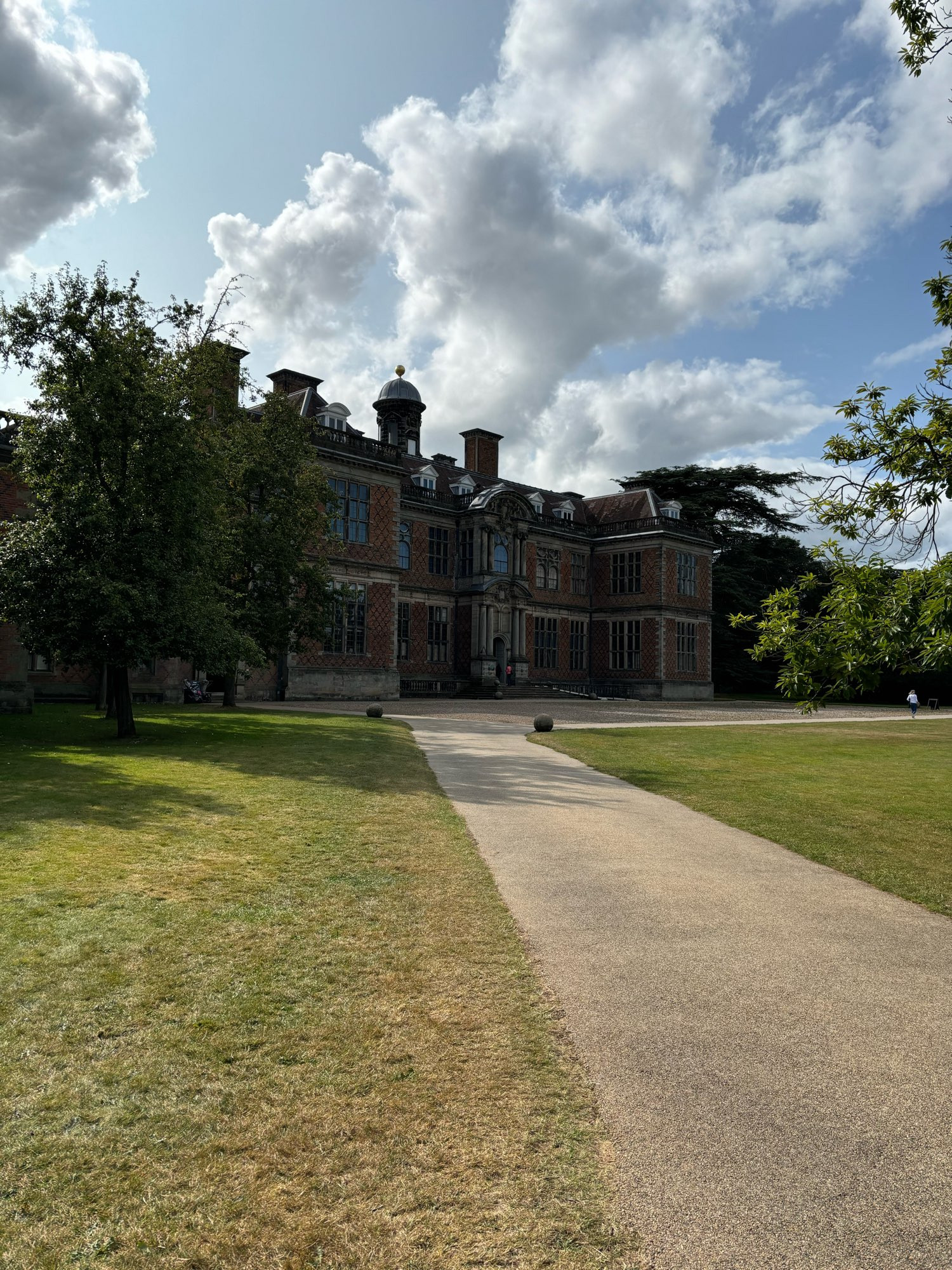 A stately home in the distance with a yellow path and green lawn in the front. Blue skies and clouds in the tip third