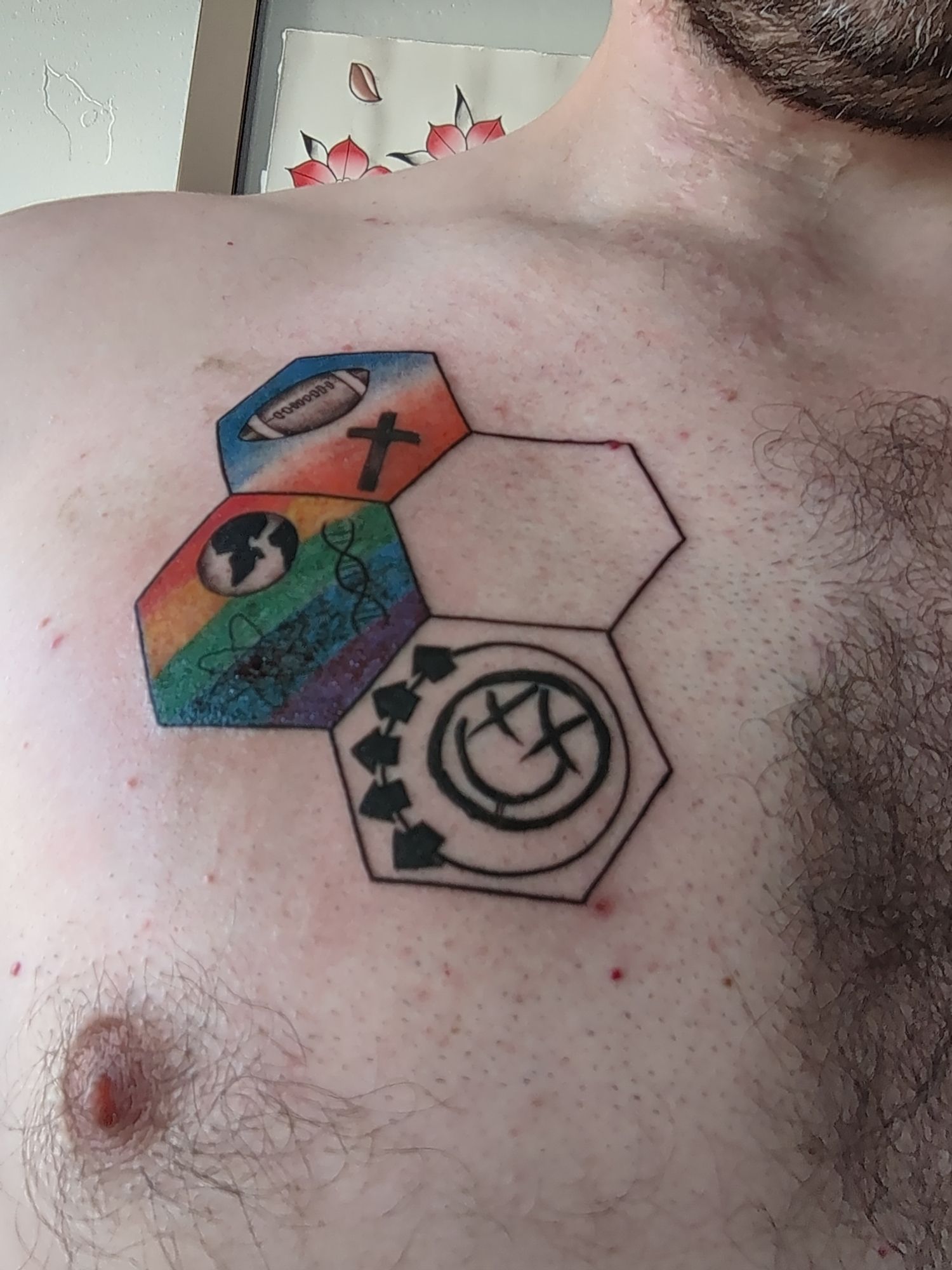 A tattoo of four hexagons with different things in each one. The first has a cross and a football with a blue and orange background. The second is blank. The third has a silhouette of earth, a DNA double helix, and a planetary model of an atom with a rainbow background. The fourth has the Blink-182 smiley face logo on a blank background.