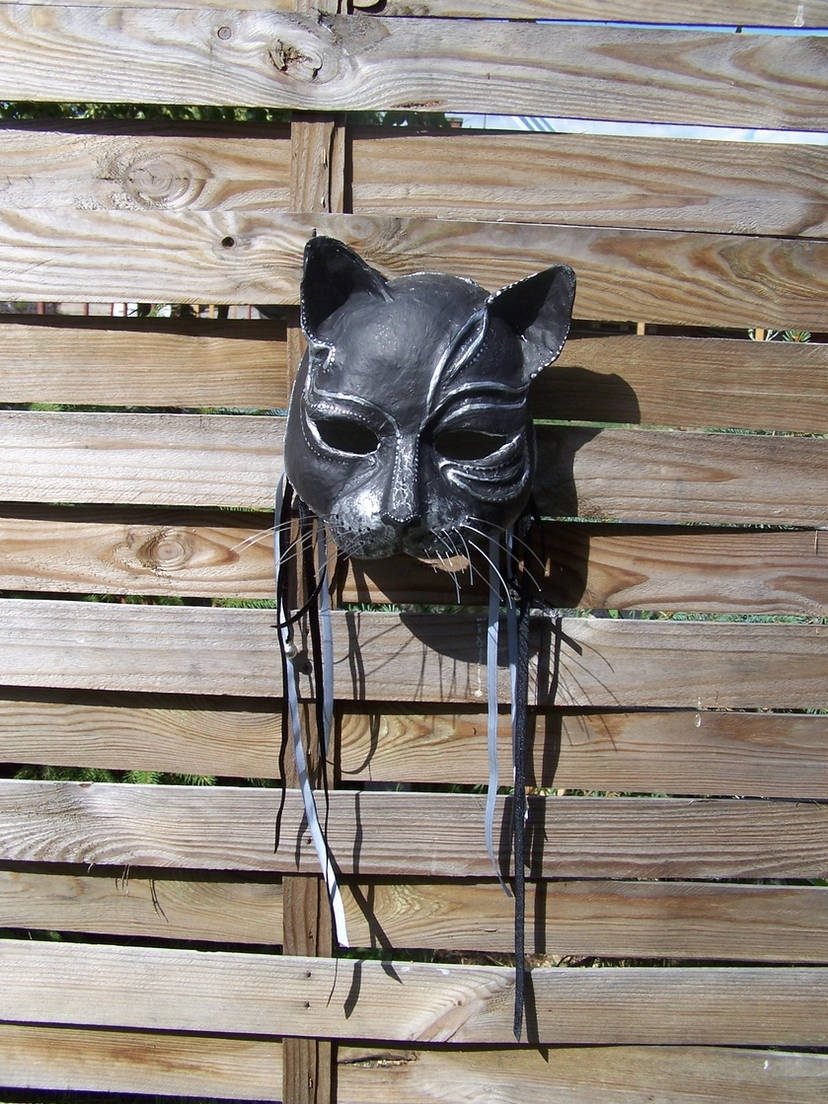 Paper mache fantasy mask of a cat, painted black and silver, with ribbons attached