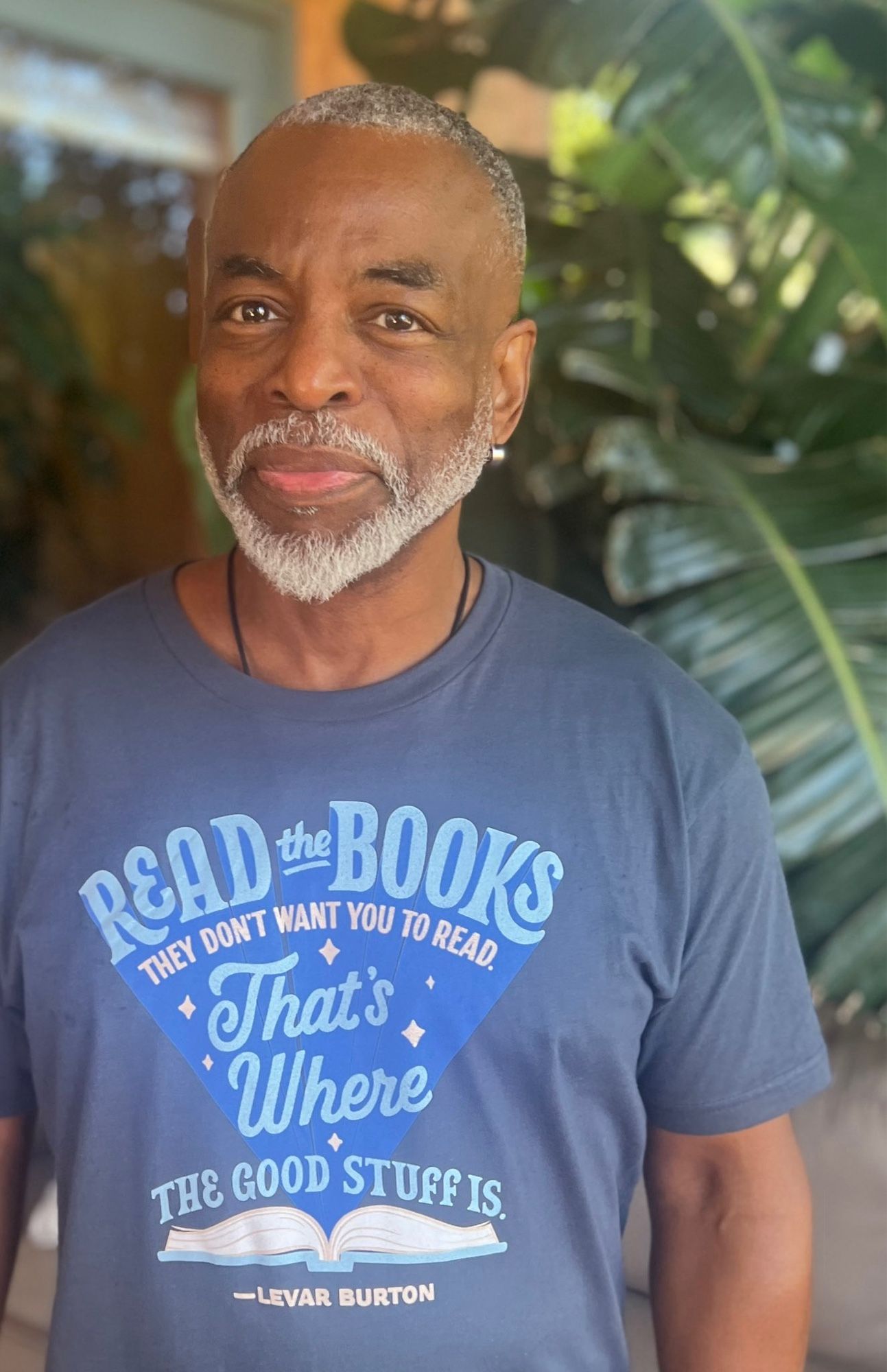 Levar Burton wearing a blue t shirt that says “read the books they don’t want you to read. That’s where the food stuff is. —Levar Burton”