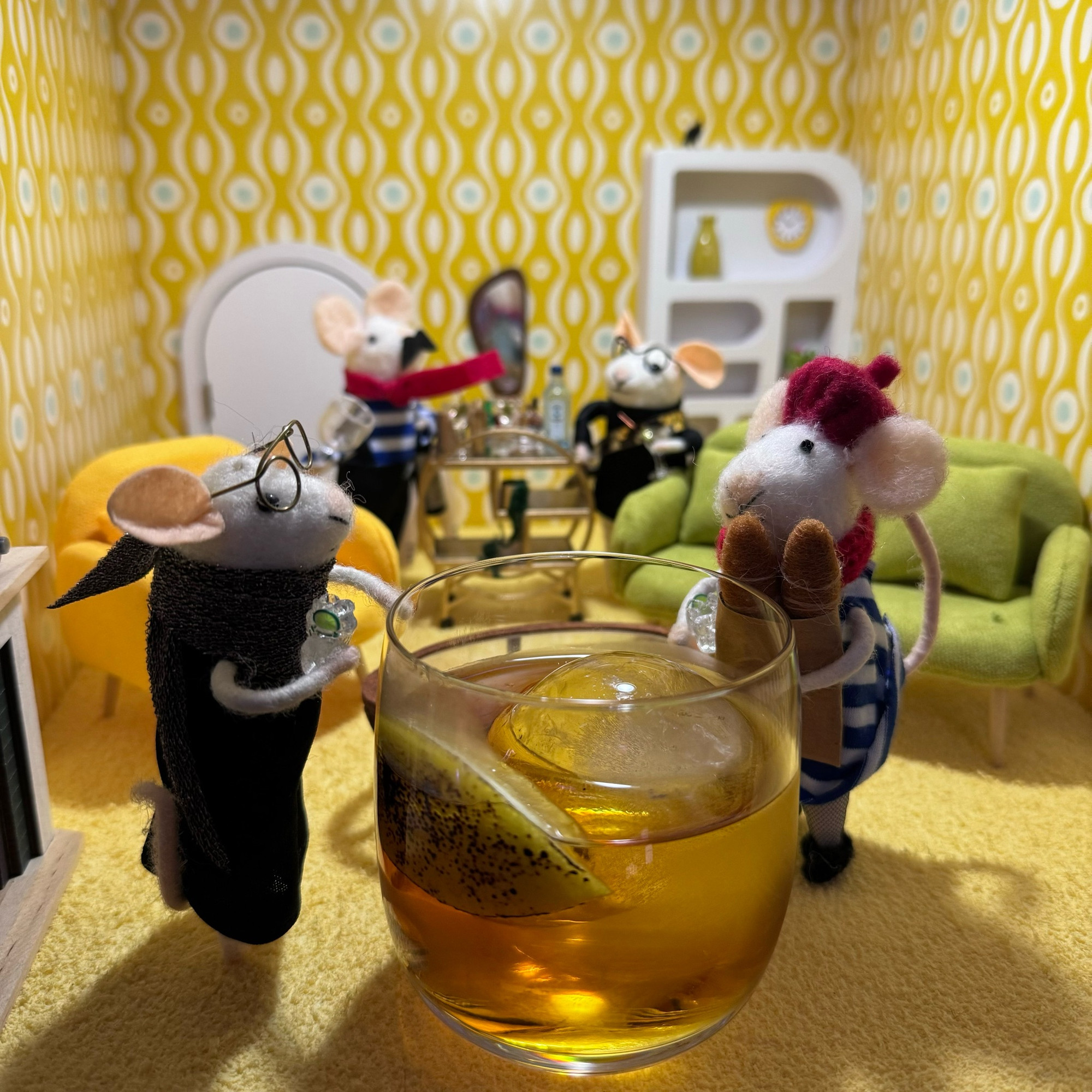 Two female felt mice leaning on a large, golden cocktail. Two male mice chat by a drinks trolley in the background.