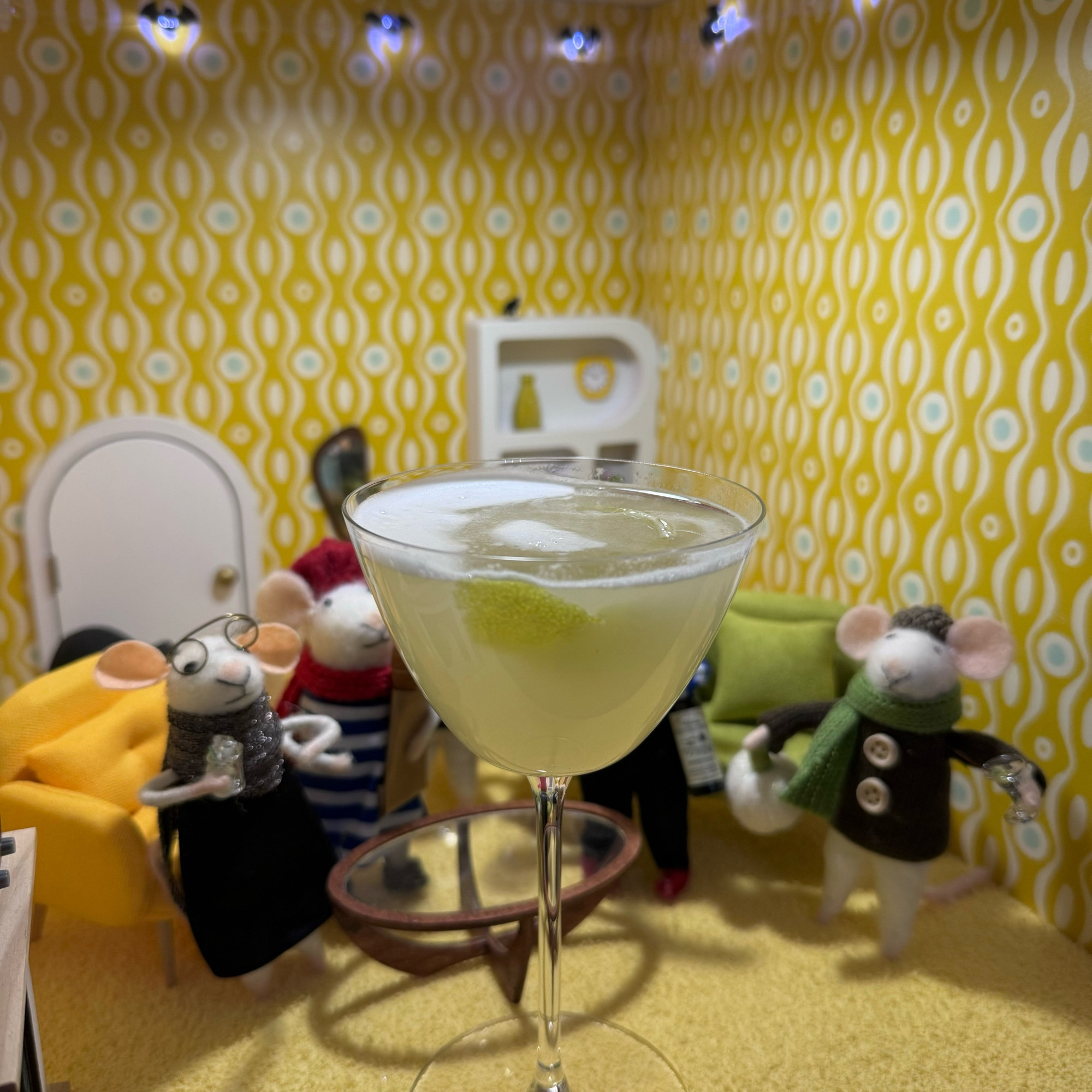 Felt mice gathered around a yellow cocktail in a very yellow room.