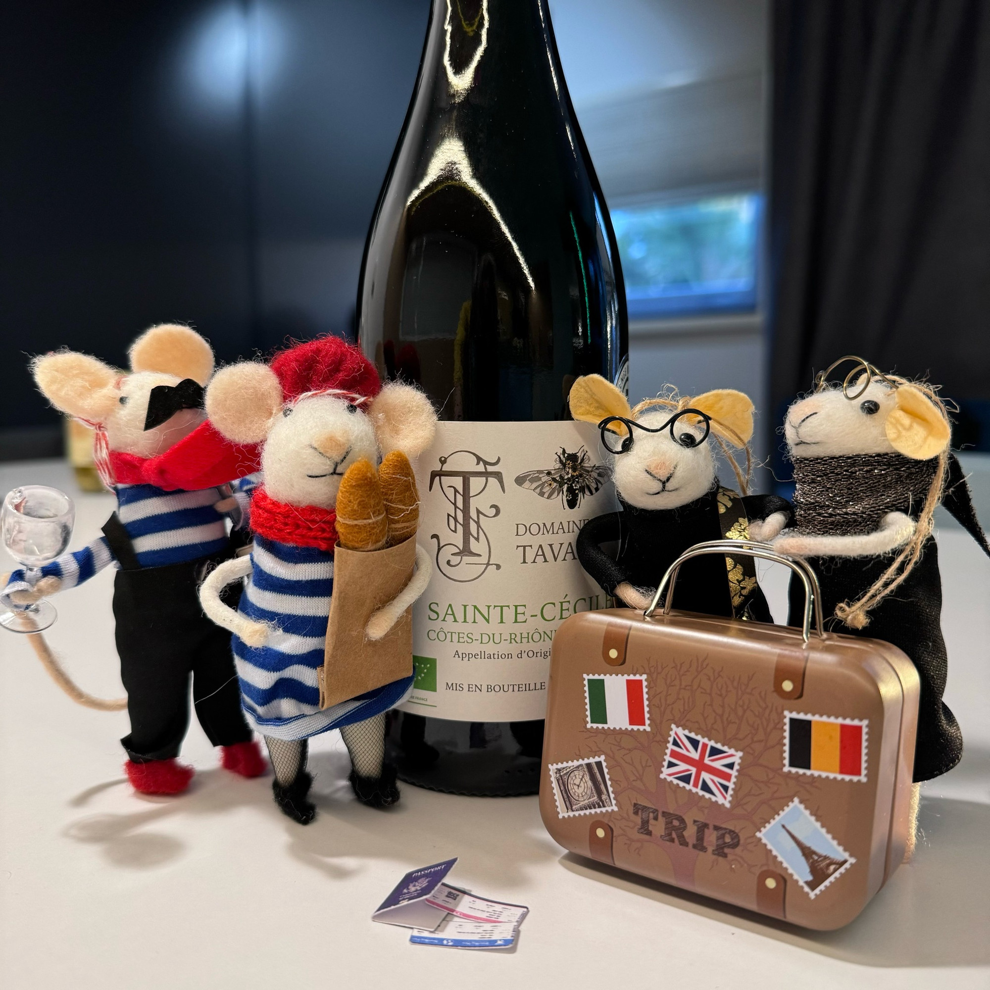 Four felt mice with a suitcase, passport and Eurostar tickets stand in front of a bottle of wine.