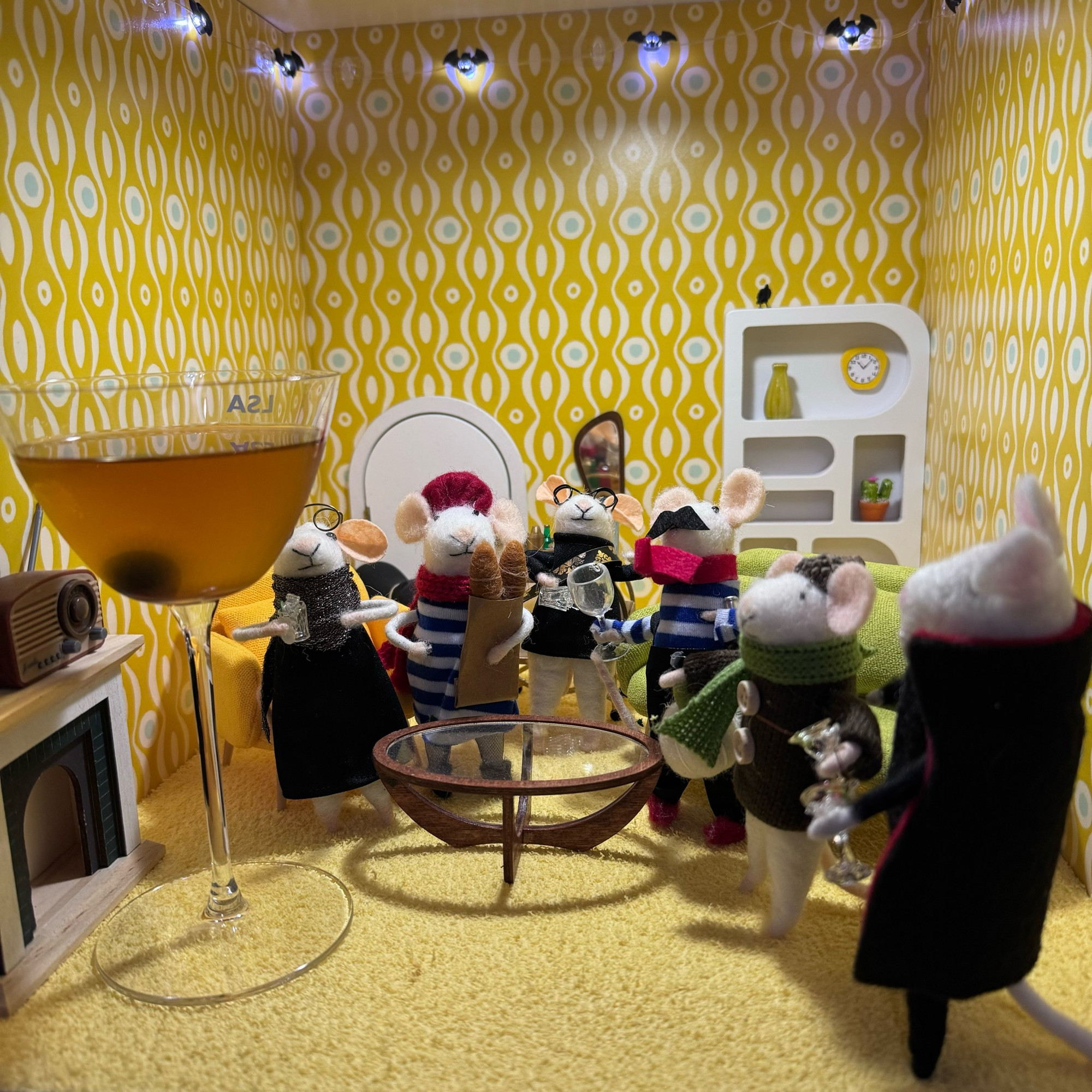 Six felt mice enjoying mouse-sized cocktails while a human-sized cocktail dominates the room.