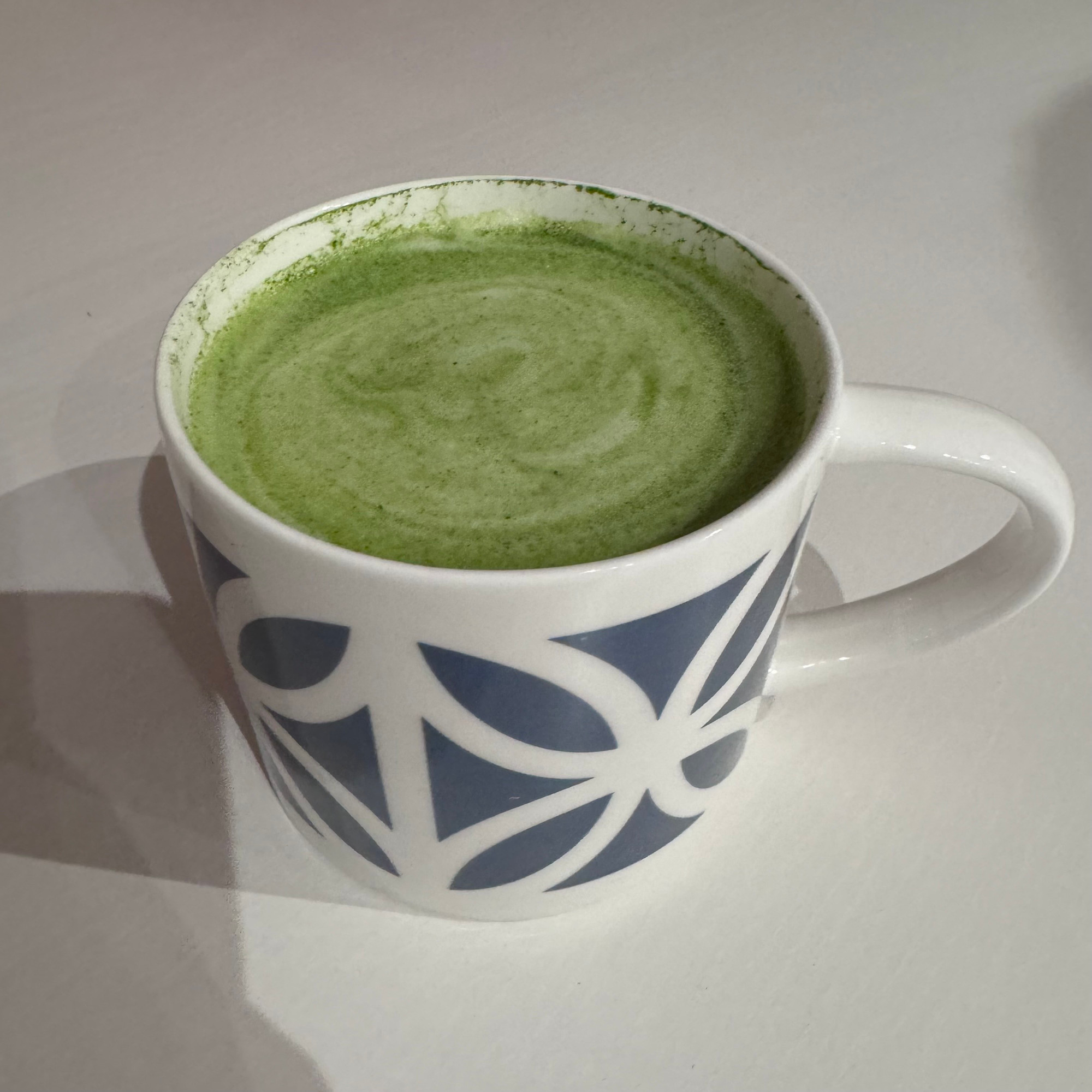 A matcha latte in a blue and white mug which bears the petal pattern out of off of concrete screen block walls.