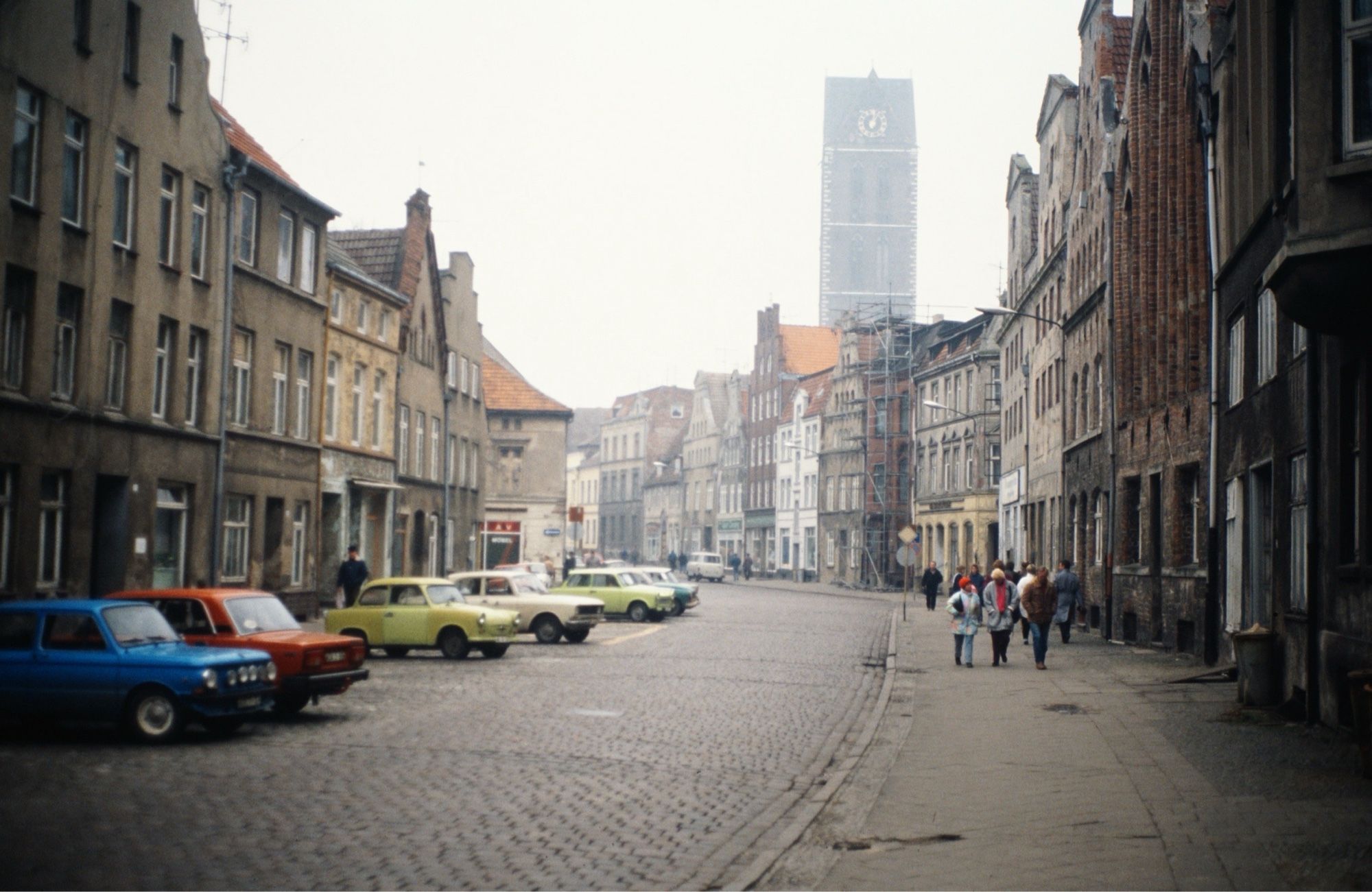 Eine Straße mit Kopfsteinpflaster und graue Häuser, im Hintergrund eine Kirche