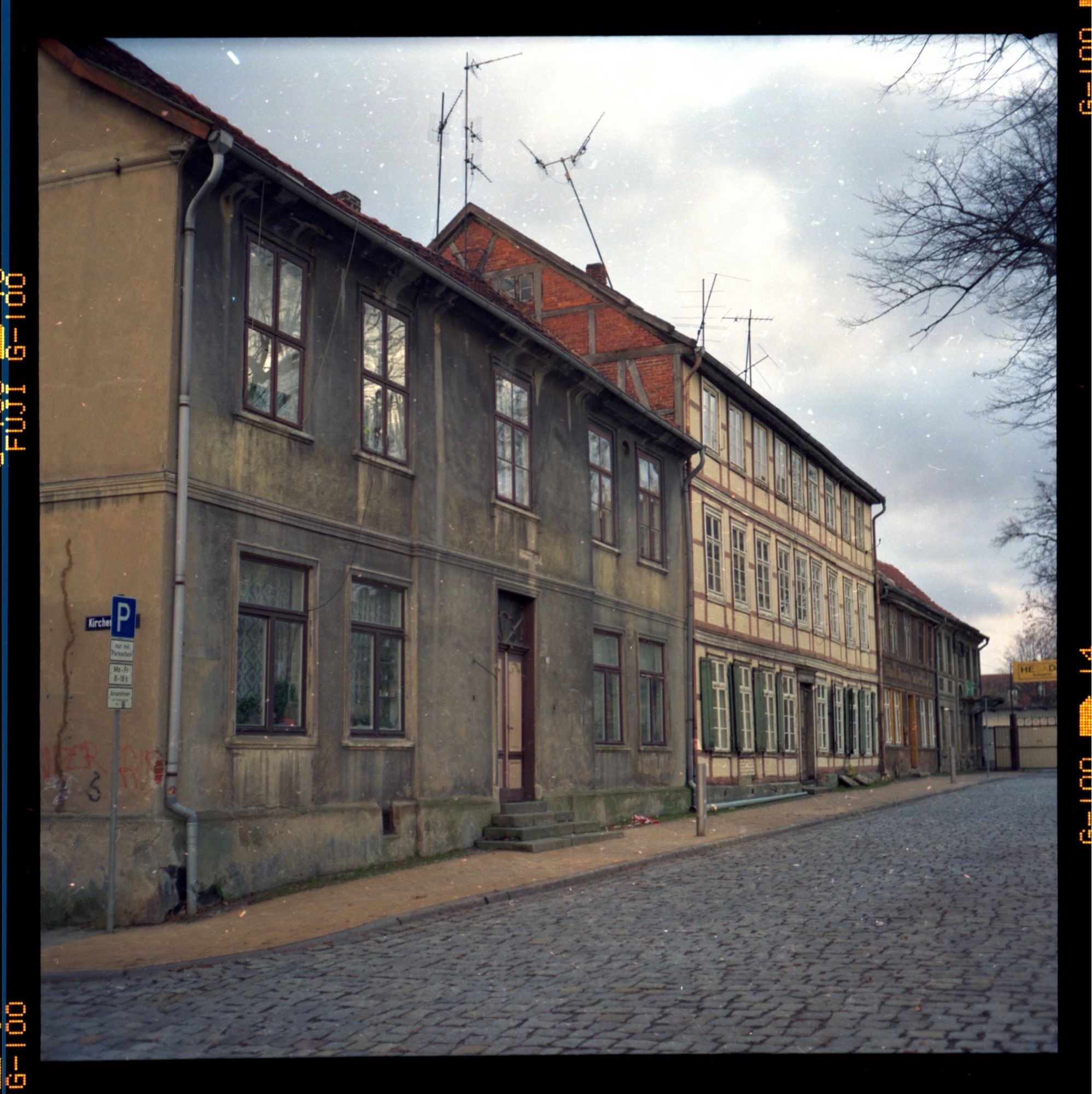 Ein paar Vorkriegshäuser mit grauer Fassade, davor Kopfsteinpflaster in der Abendsonne