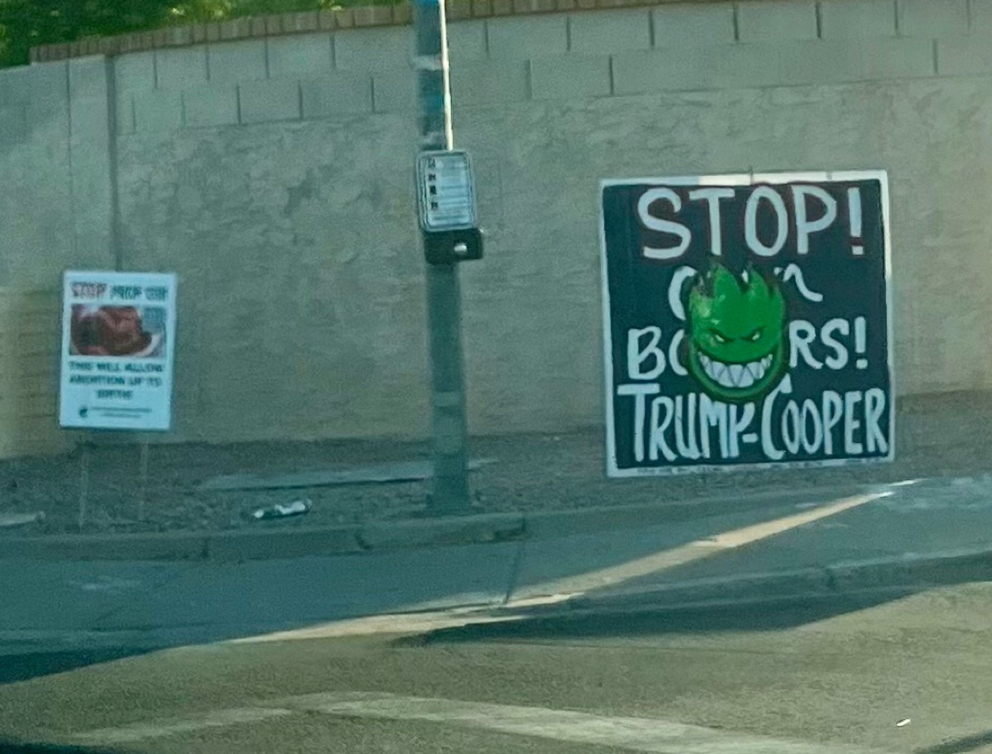 A DIY sign along the road that’s just plain black paint with white text reading “stop open borders, Trump-cooper”

someone has placed a large green Spitefire smiling flame logo in the dead center, covering half the text