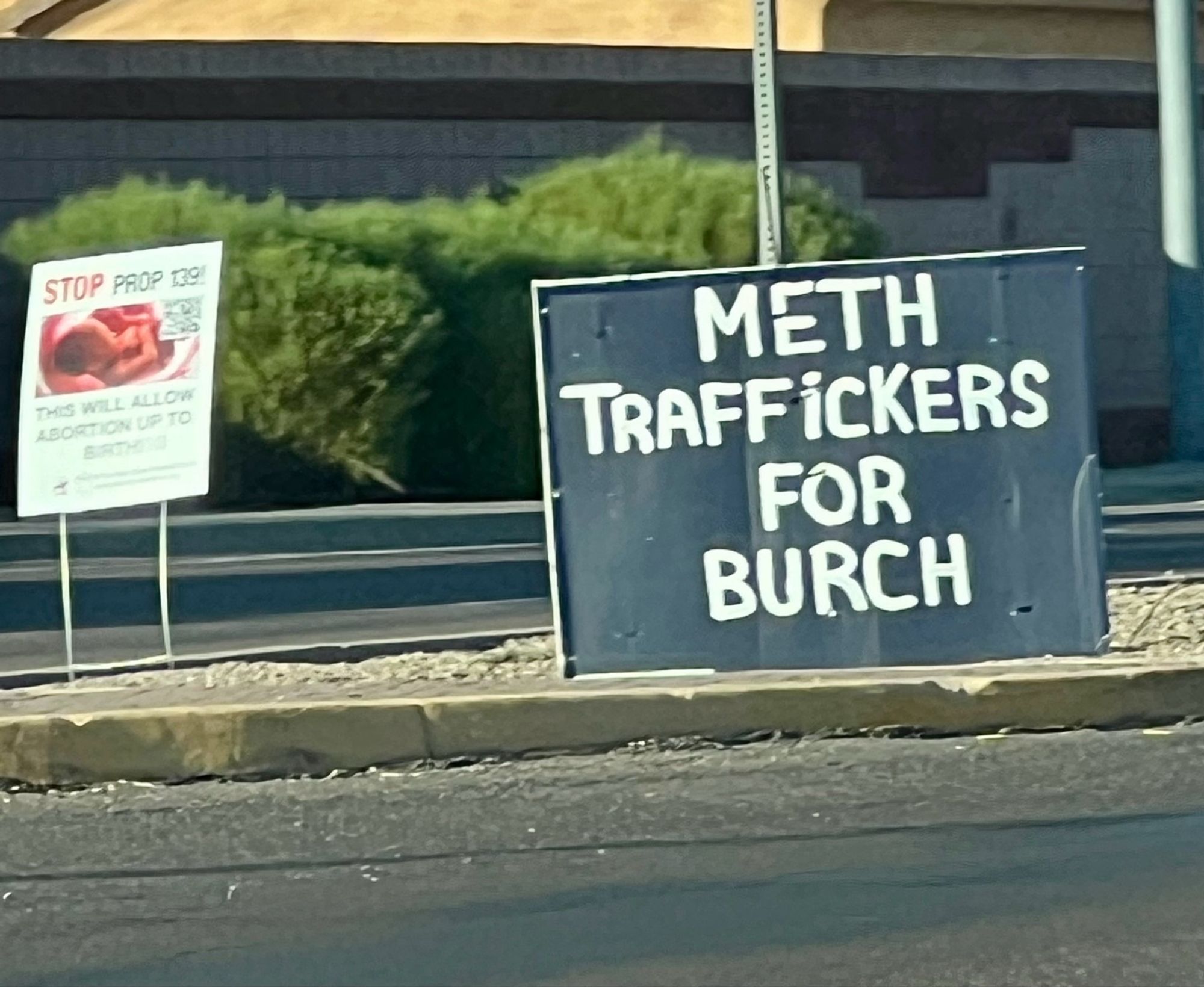 A DIY sign along the road that’s just plain black paint with white text reading “METH TRAFFICKERS FOR BURCH”