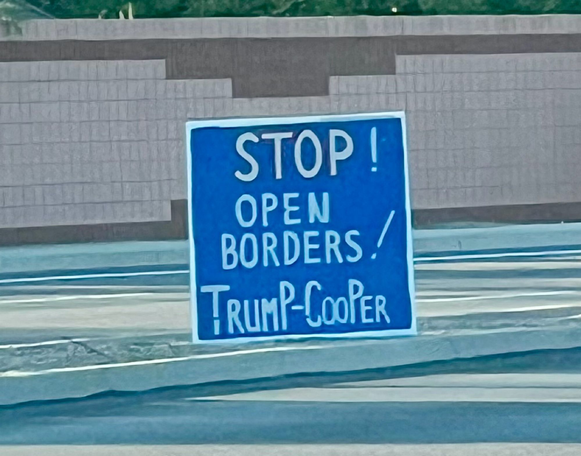 A DIY sign along the road that’s just plain blue paint with white text reading “stop open borders! Trump-Cooper”