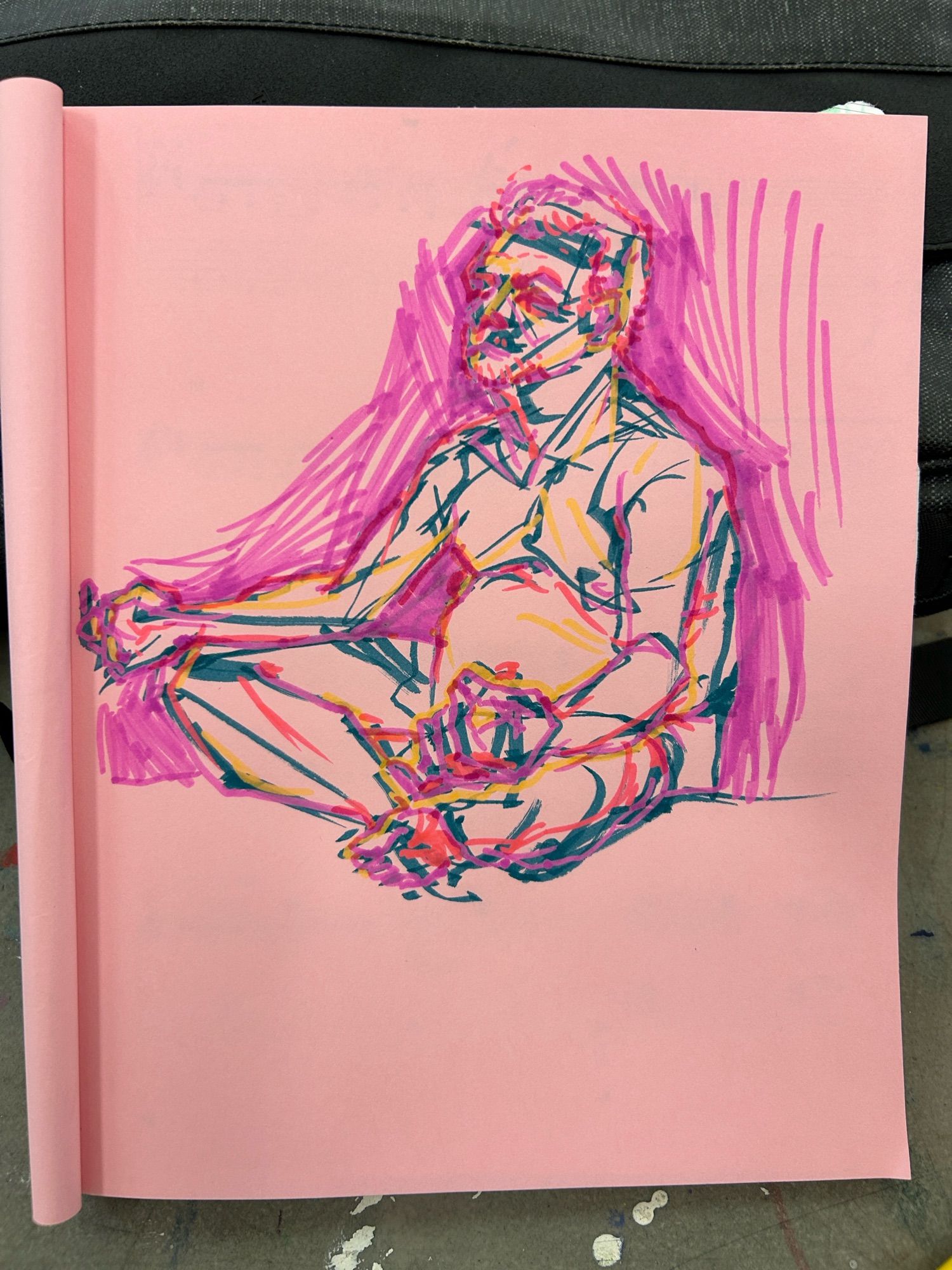 On pink sketchbook paper, a marker sketch of a nude man with his legs crossed and resting his arms on them