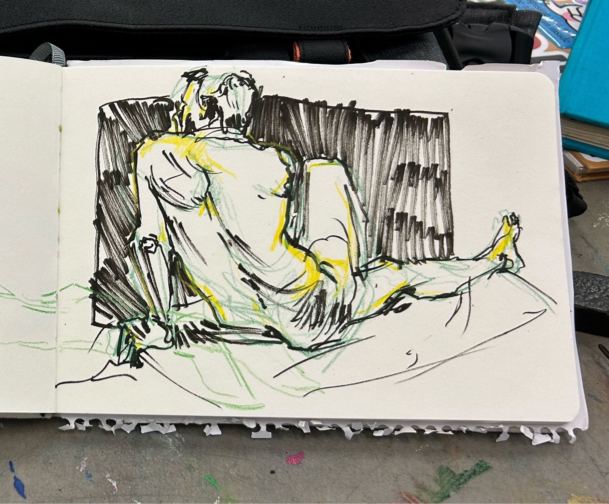 Sketch of a nude man sitting on a platform, looking to the left and supporting himself with his left arm, with his right leg crossing over his fully extended left leg. Done with a black marker, with green and yellow colored pencil accents.