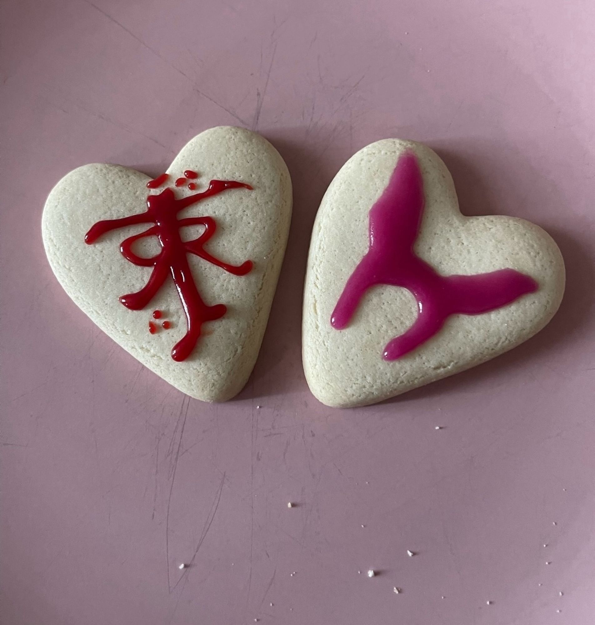 throwback to some biscuits i decorated well over a year ago. they are two heart shaped beige biscuits. on the left, in red icing, i drew j r r tolkien’s signature thing. it’s one big J which is also a T. along the stem is two R’s mirroring one another on each side. i nailed it tbh. on the right is louise belcher’s pink bunny hair. fucking nailed that too. they’re on a pink plate and a few crumbs dotted about below