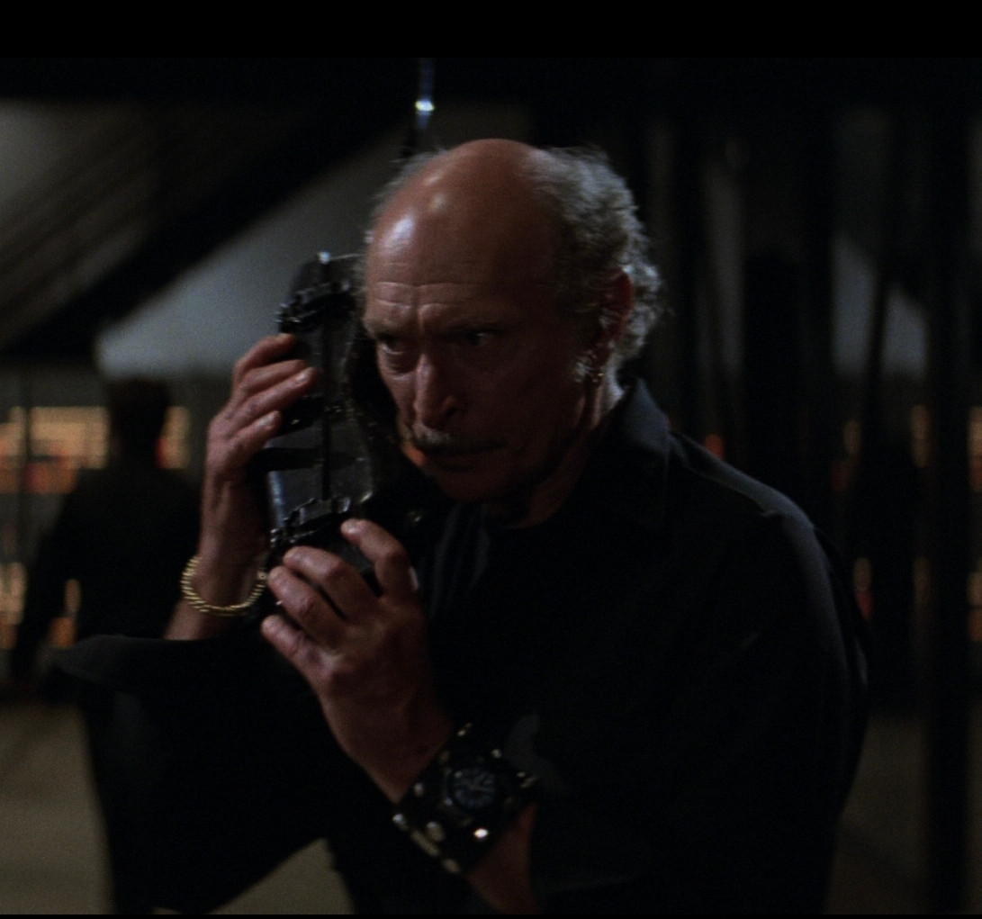 Scene from Escape From New York with police commissioner holding a comically large all black wireless telephone up to his face. 