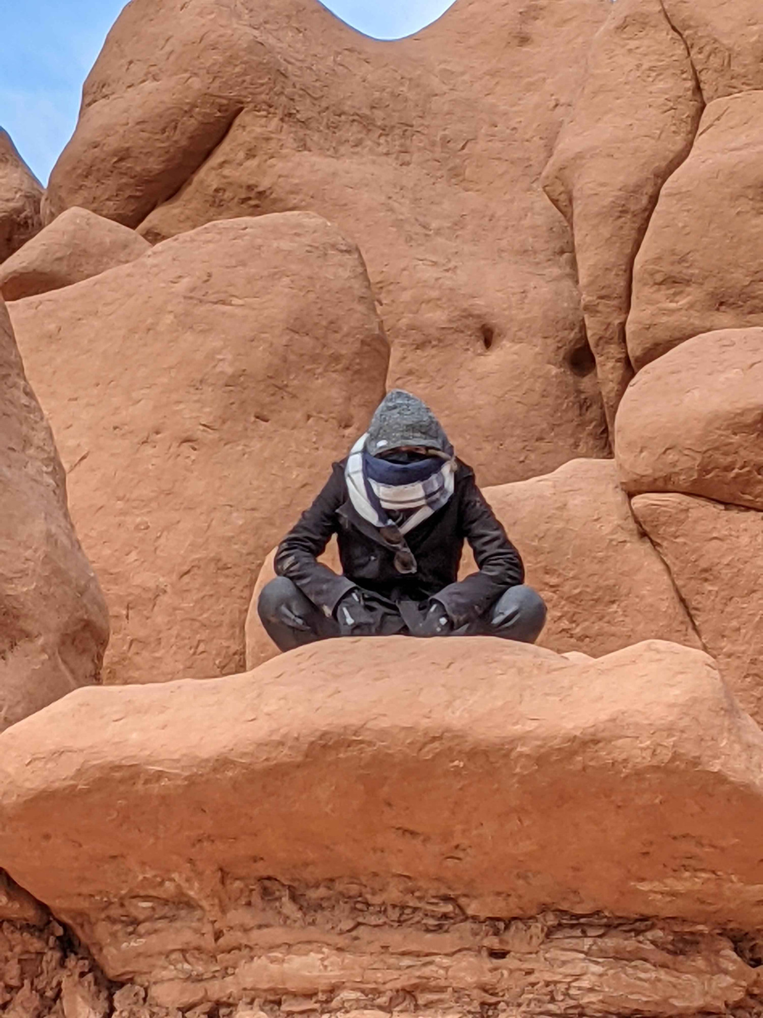 A mysterious NPC perches upon the slab of malformed sandstone above. Their form and face remain obscured, save their eyes - but within lies a glint of well-worn secrets, a passive expectation in the curve of their shoulders. There is no rush out here. No, not beneath this beating sun and too-clear sky. The empty blue presses in, threatens to swallow any not huddled in the safety of the mangled sandstone.

The black-clad silhouette and gritty red stone couldn't look more disparate, but they sit as motionless as if they'd been formed of the same clay. As if this stranger, borne of this perch, has been here long before time held meaning. And will persist long after. In their patience, figure and stone are one.

You may not have need of this stranger now. But they remain.
You will know when the time is right. She will be waiting.