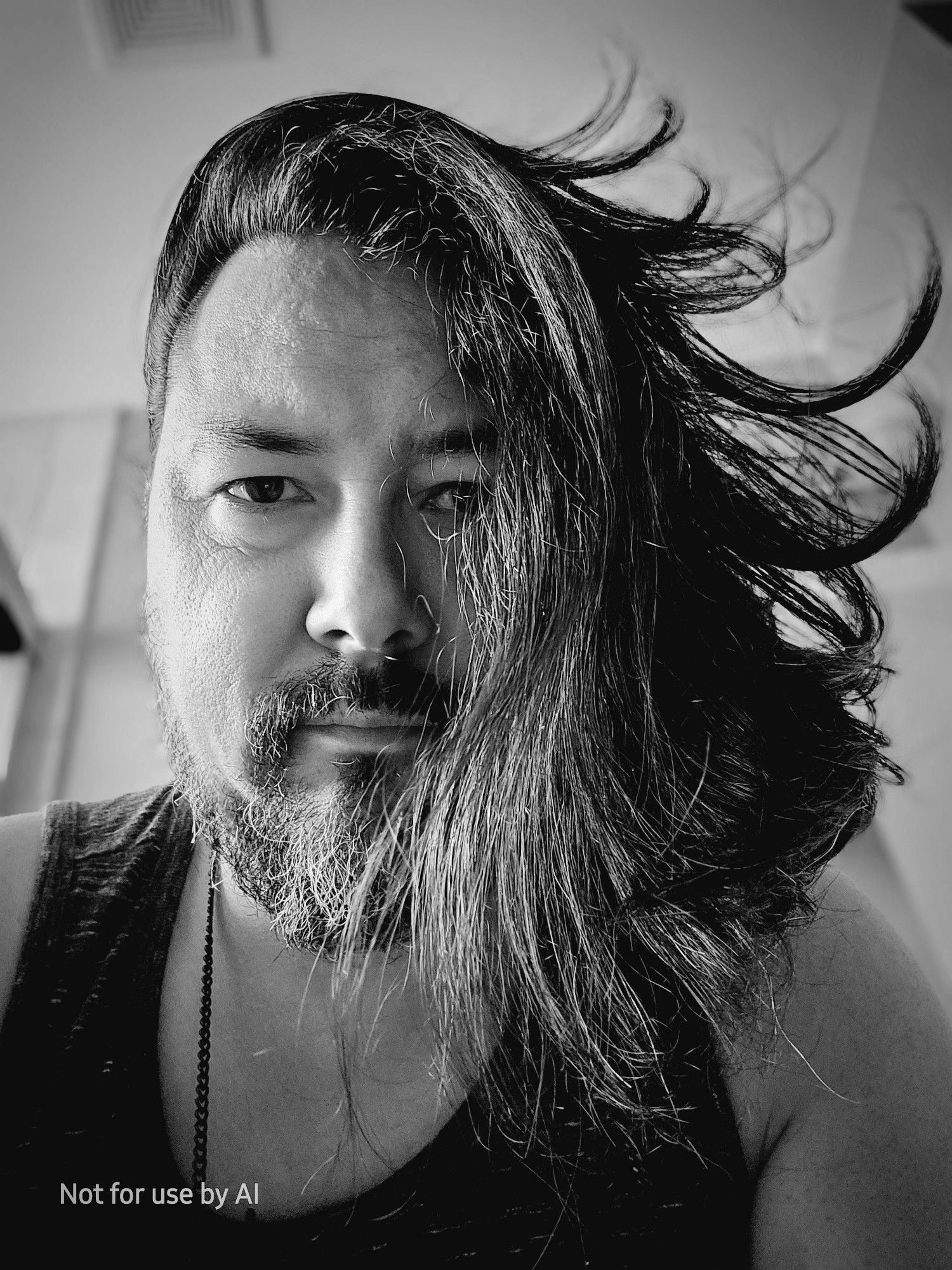 A black-and-white, vignette-shaded picture of me, a 46-year-old, queer, cisgender, biracial (Japanese | Anglo European) male human with chocolate brown eyes, pepper-and-salt hair, & salt-and-pepper facial hair. I am looking down at the camera, ans all my hair is swept up and over to one side.