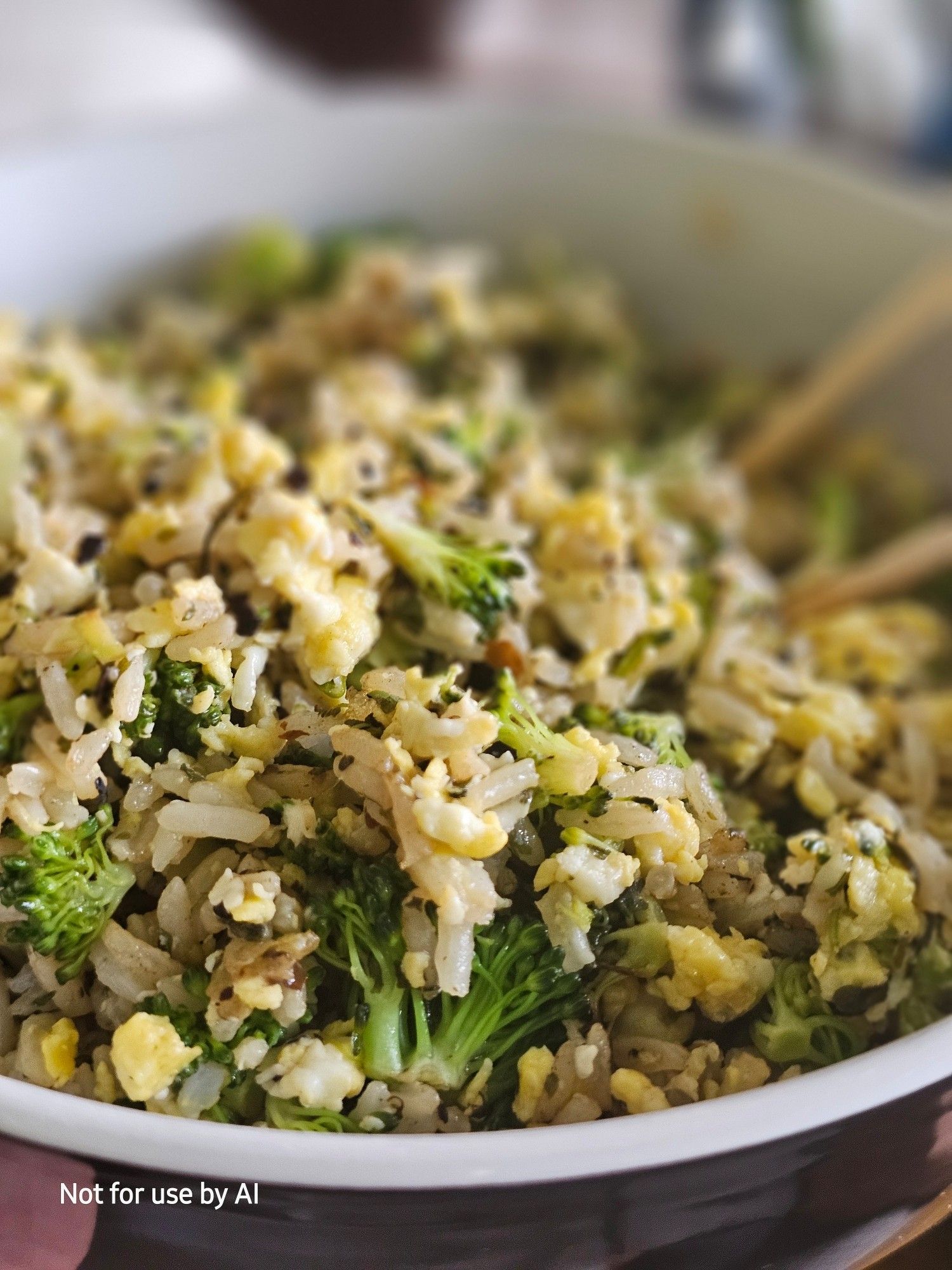 A closeup shot of fresh broccoli that's been finely chopped, sautéed in olive oil, parsley, & urfu biber pepper, tossed with white rice, and then scrambled with egg, in a white bowl glazed in black on the outside.