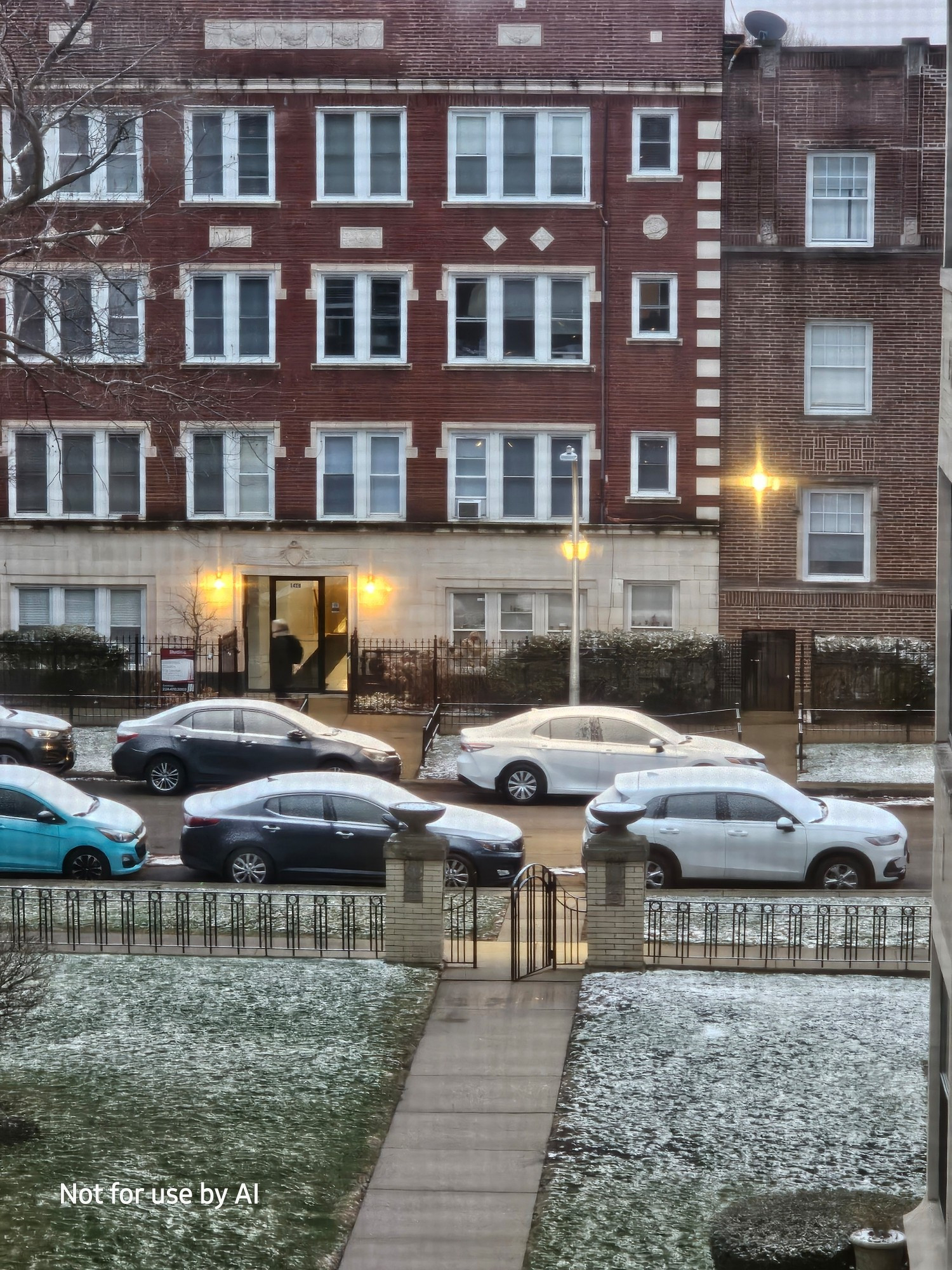 A closeup of the cars out on the street in front of our building, lightly dusted with snow. There is a watermark in the lower lefthand corner that reads, "Not for use by AI".