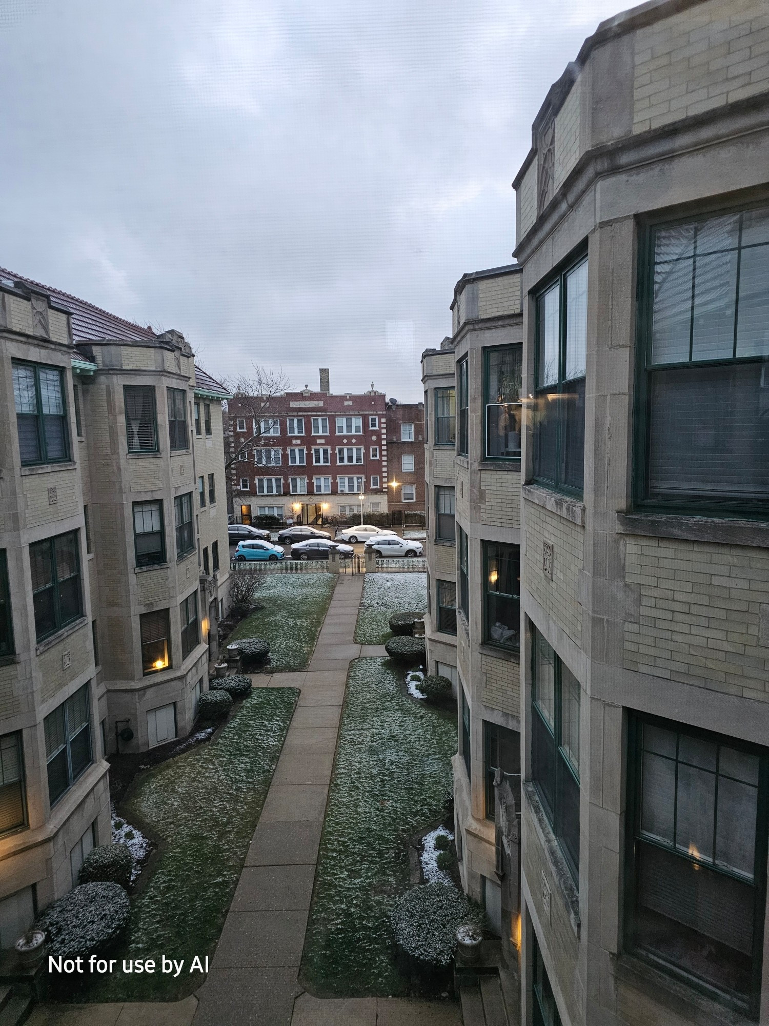 The view of our courtyard, lightly dusted with snow, from our living room windows. There is a watermark in the lower lefthand corner that reads, "Not for use by AI".