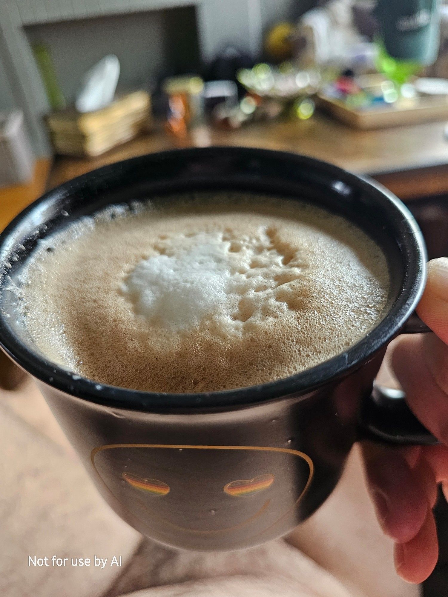 Me holding a black mug with a golden smiley face with heart-shaped, Pride-colored eyes, filled with a homemade, dark chocolate, coconut mocha. There is a watermark in the lower lefthand corner that reads, "Not for use by AI".