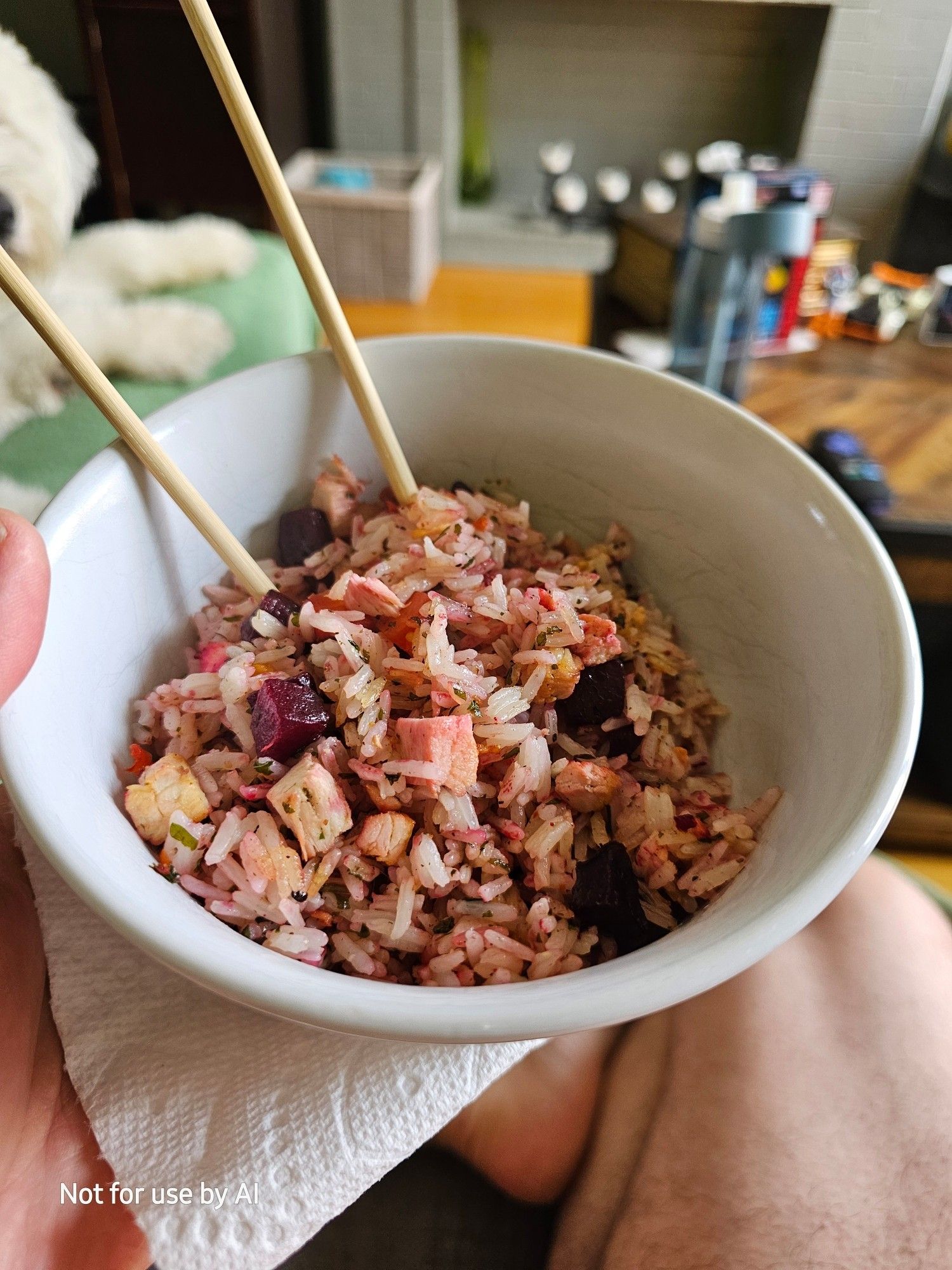 Roast chicken, carrots, & beets, & white rice, that has been sautéed in a pan with olive oil, dried parsley, & freshly-cracked black pepper, & then put in a simple, white bowl with a pair of wooden chopsticks. There is a watermark in the lower lefthand corner that reads, "Not for use by AI".