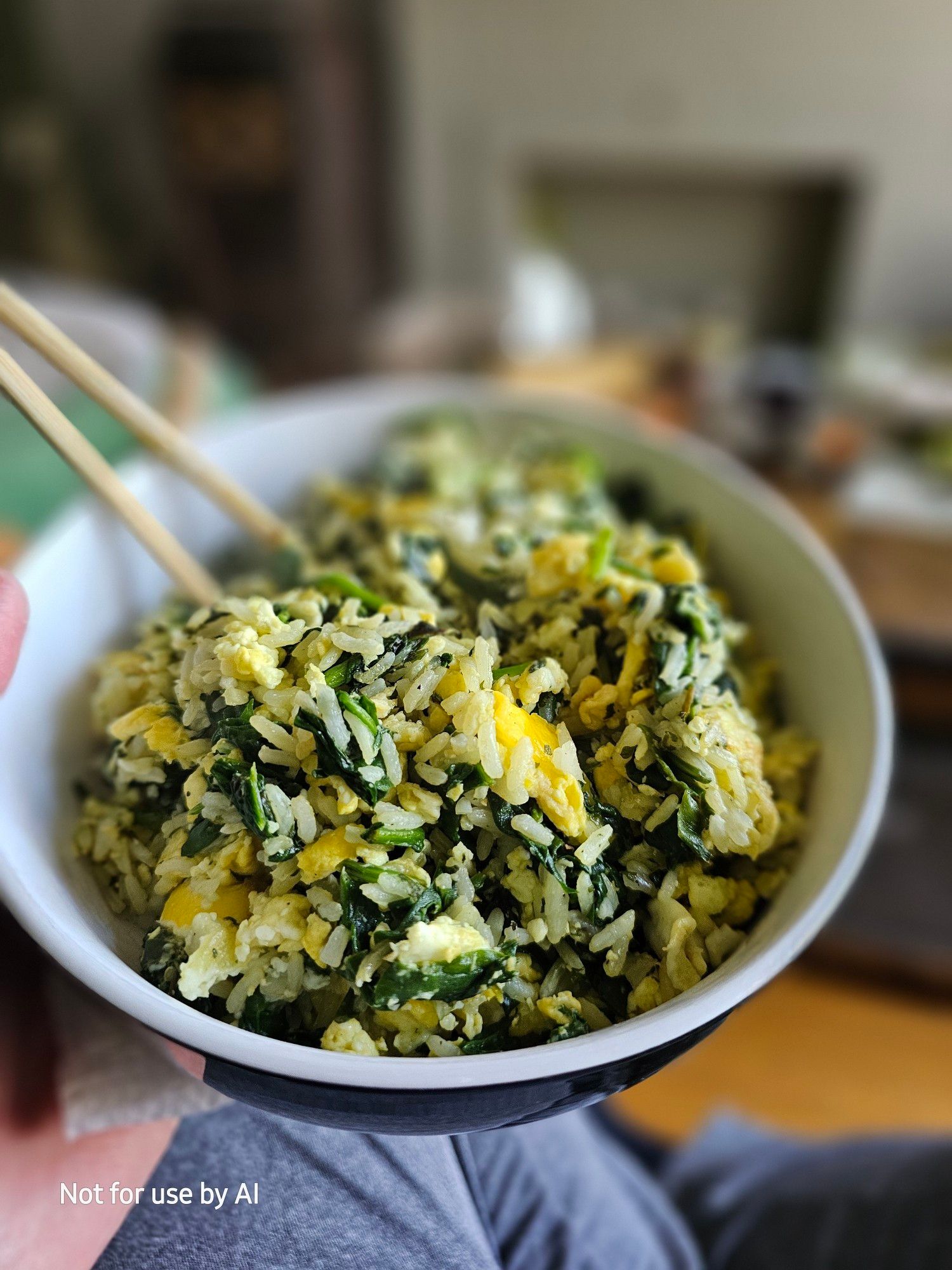 Spinach sautéed in olive oil with freshly-cracked black pepper, dried parsley, and white rice, and then tossed with scrambled eggs, in a white bowl with a black outside. There is a watermark in the lower lefthand corner that reads, "Not for use by AI".