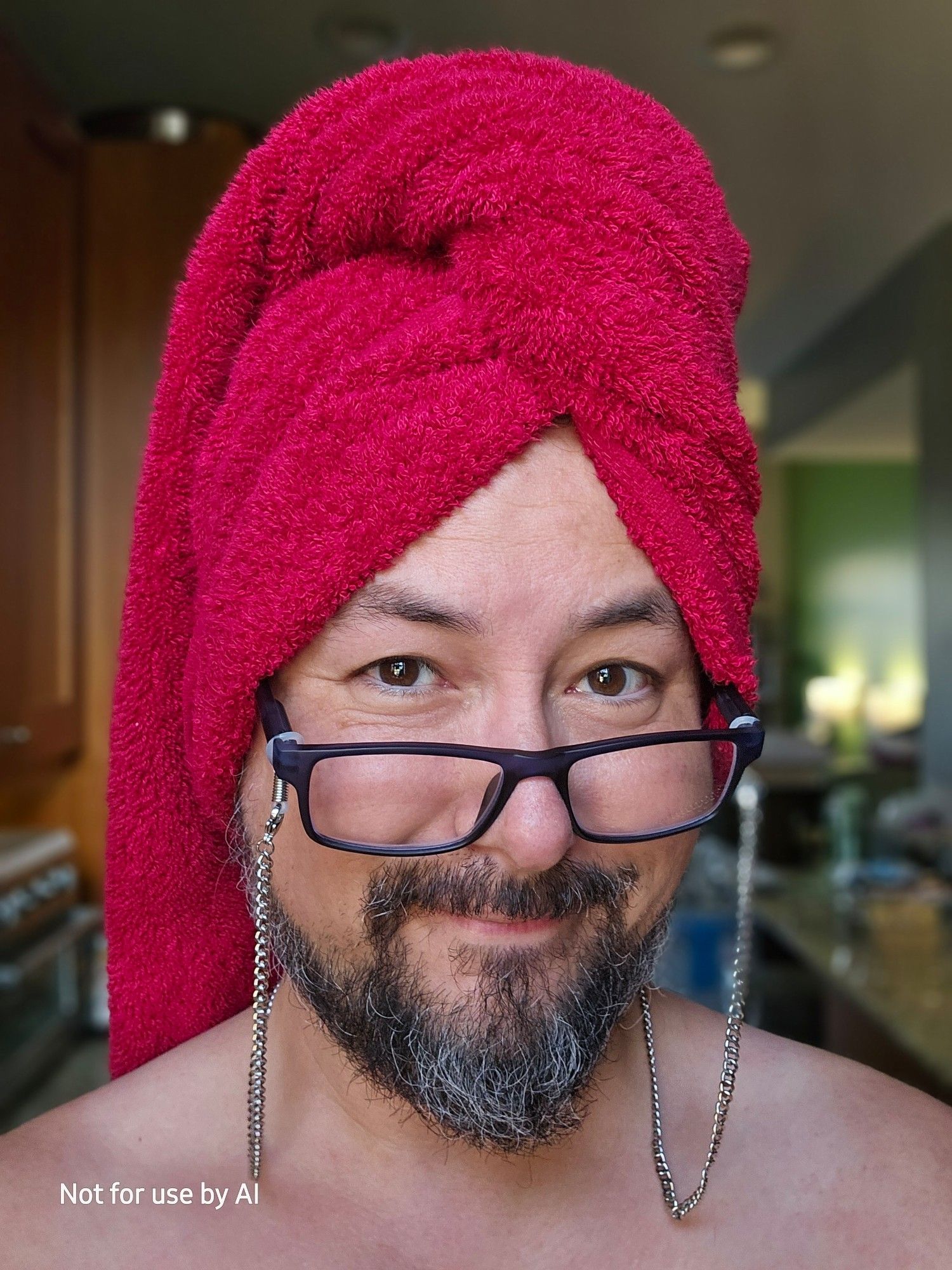 Me standing in our kitchen, naked, with a red towel wrapped around my freshly-washed hair, and smiling at the camera over my translucent blue readers, with my silver glasses chain on them.