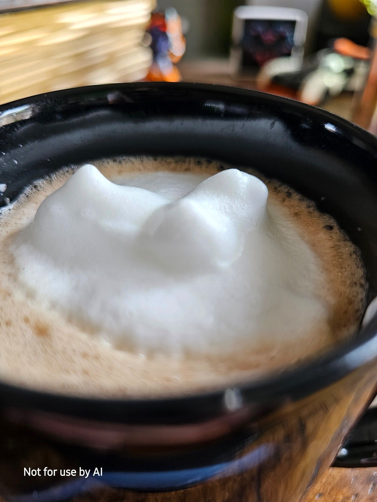 Especially light, fluffy, foamy foam floating atop a homemade, coconut, dark chocolate mocha in a black mug. There is a watermark in the lower lefthand corner that reads, "Not for use by AI".