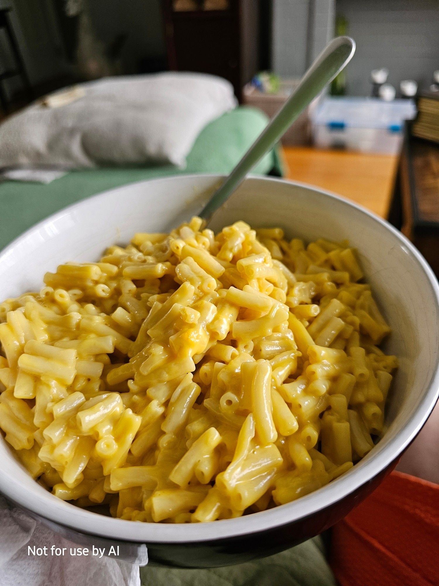 A white bowl, glazed in black on the outside, full of mac and cheese, with a spoon sticking out of it.