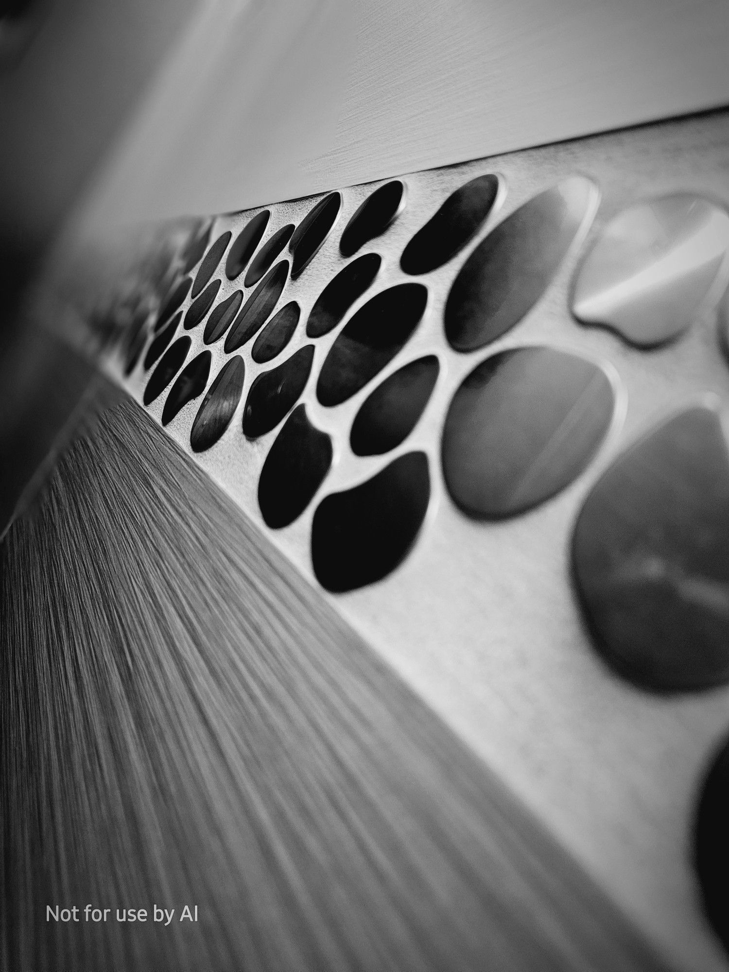 A black-and-white, vignette-shaded picture of the wall of the stall I'm sitting in, showing two different types of tiling separated by a section of brushed-nickel pieces embedded in grout to mimic stones.