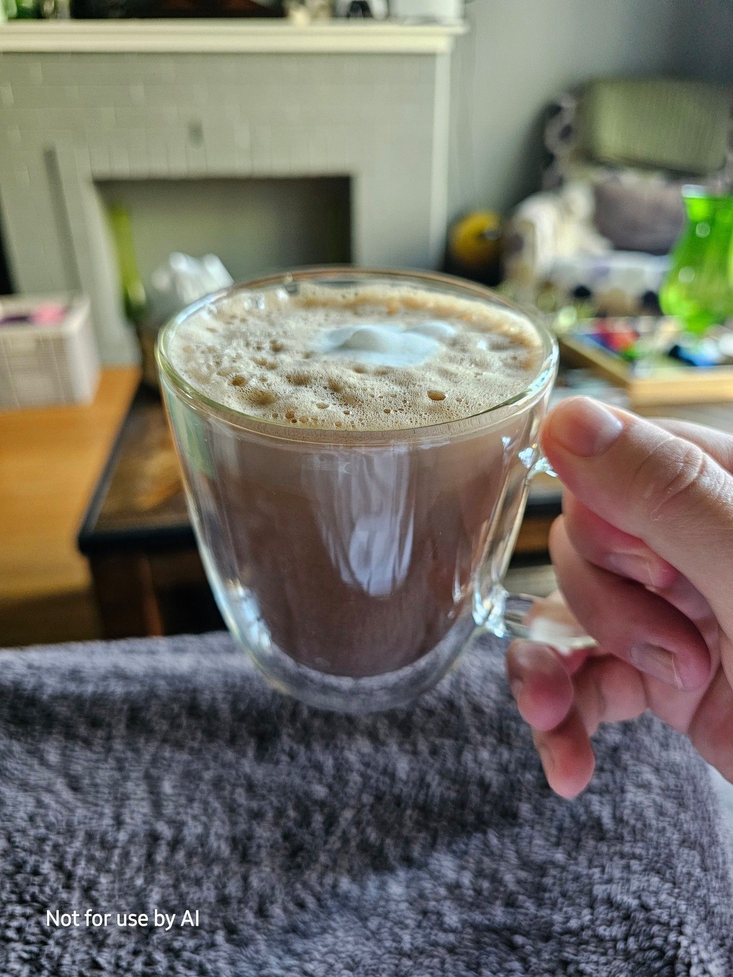 Me holding a clear, double-insulated glass mug, containing a homemade dark chocolate & coconut mocha. There is a watermark in the lower lefthand corner that reads, "Not for use by AI".