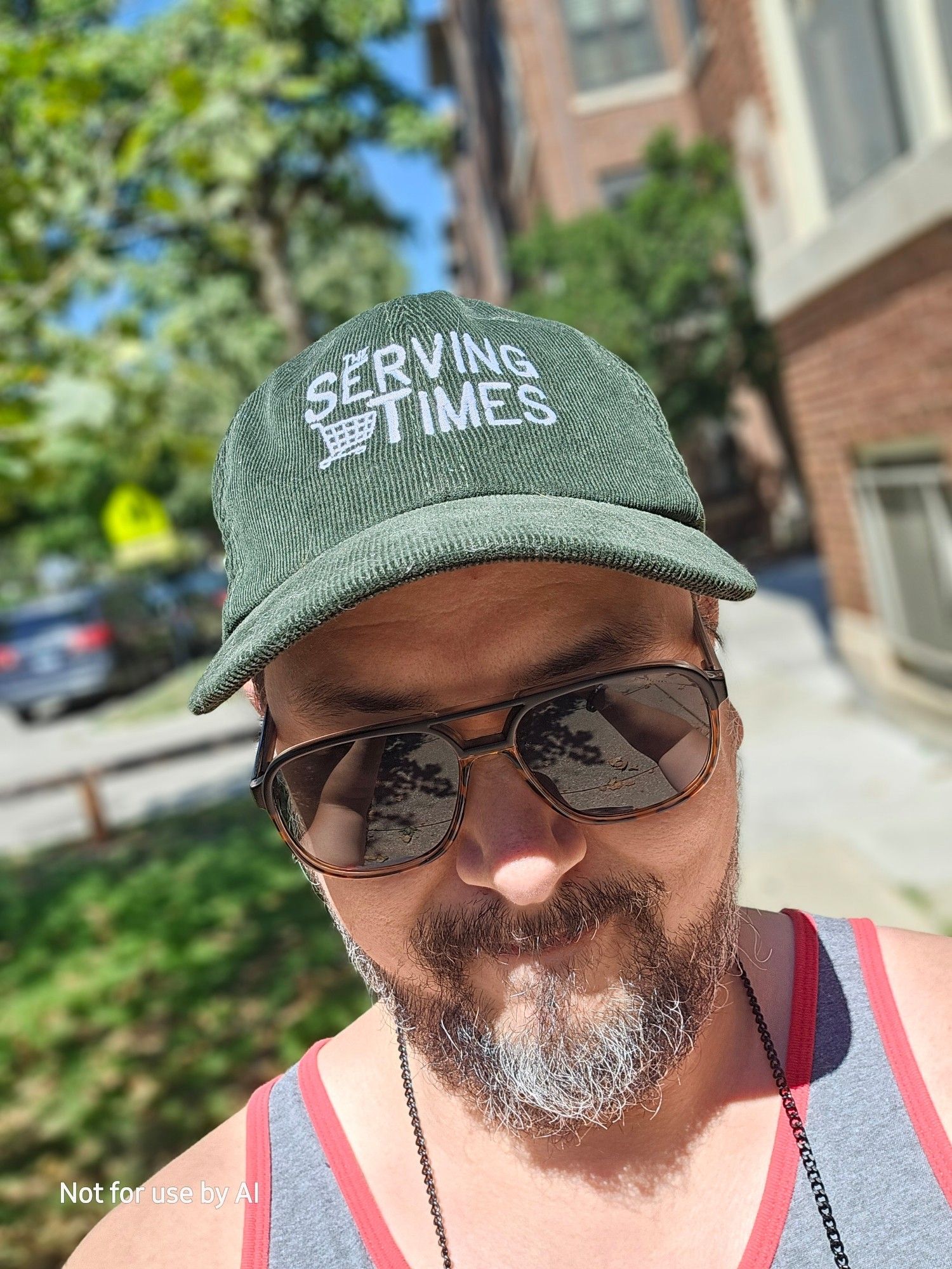 Me wearing a green,  corduroy baseball cap embroidered in white with the logo for "The Serving Times".