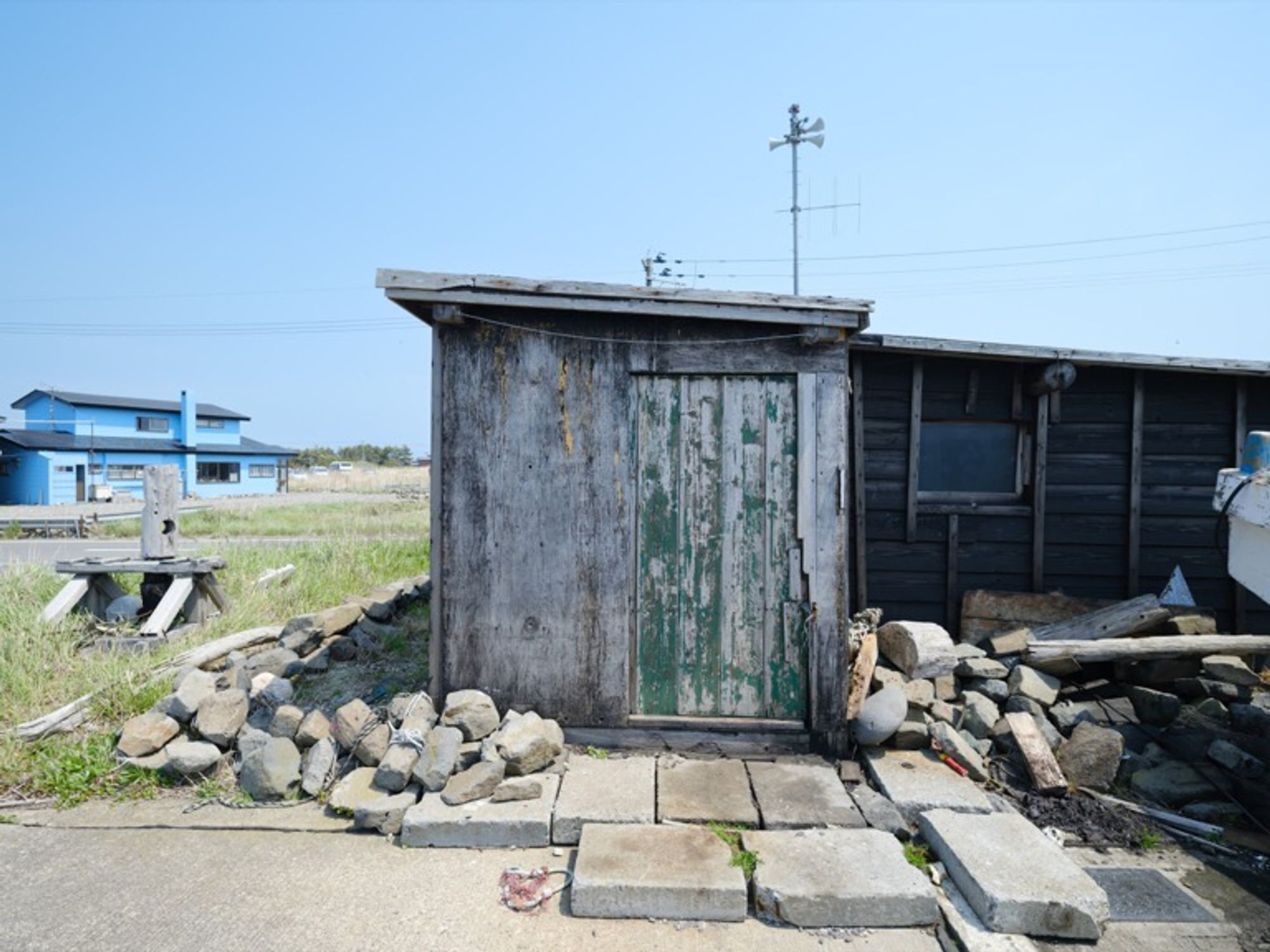 An old wooden hut on a boat landing, surrounded by cluttered stones and debris, shows signs of exposure to sea breezes, rain, snow, and high tides over the years. Captured in 2024 with the GFX100S and GF23mmF4 R LM WR. Aomori, Japan.