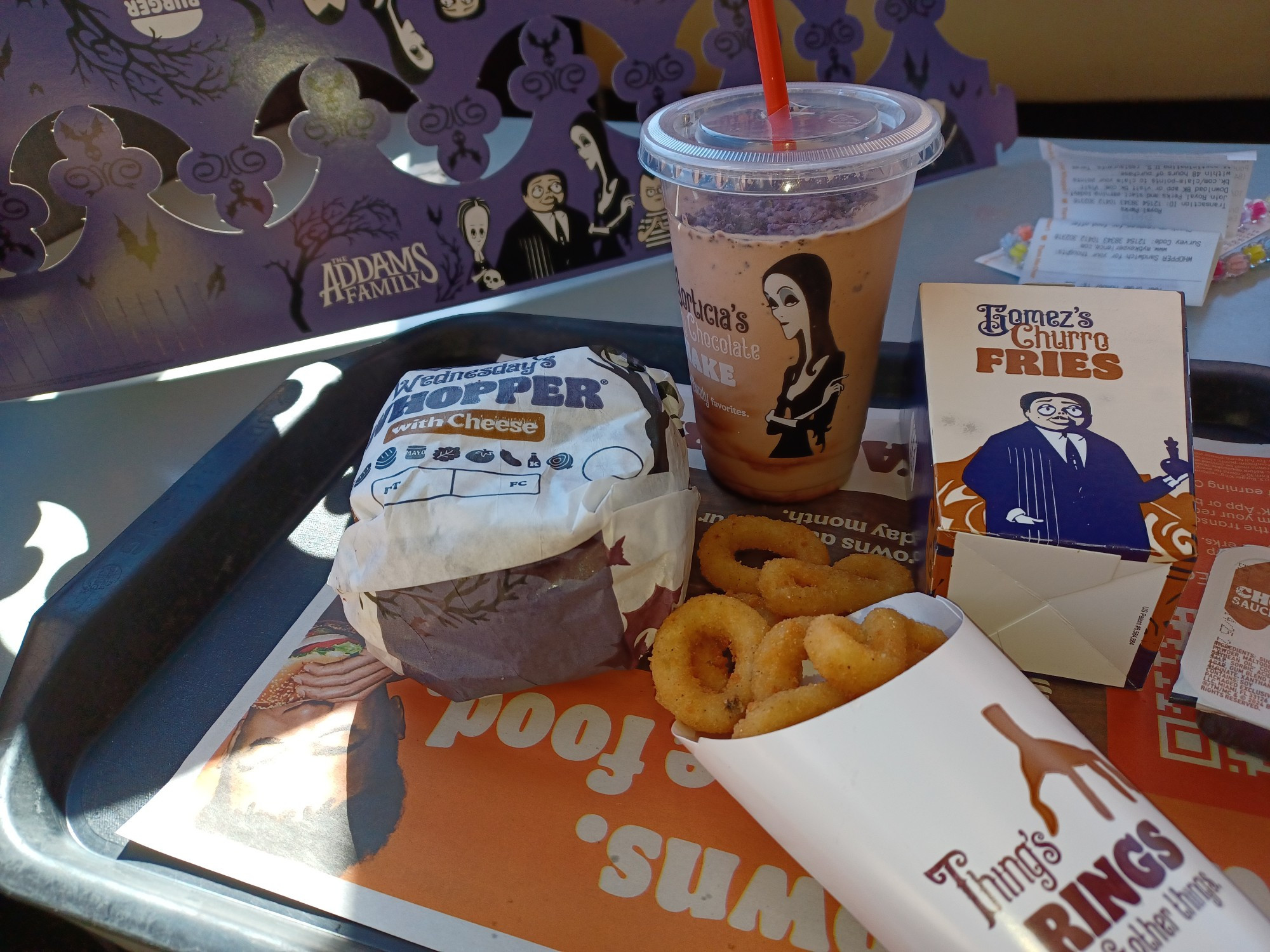 Two cardboard Addams Family crowns, a Wednesday Whopper, Thing's Onion Rings, Morticia's Kooky Shake, and Gomez's Churro Fries from Burger King