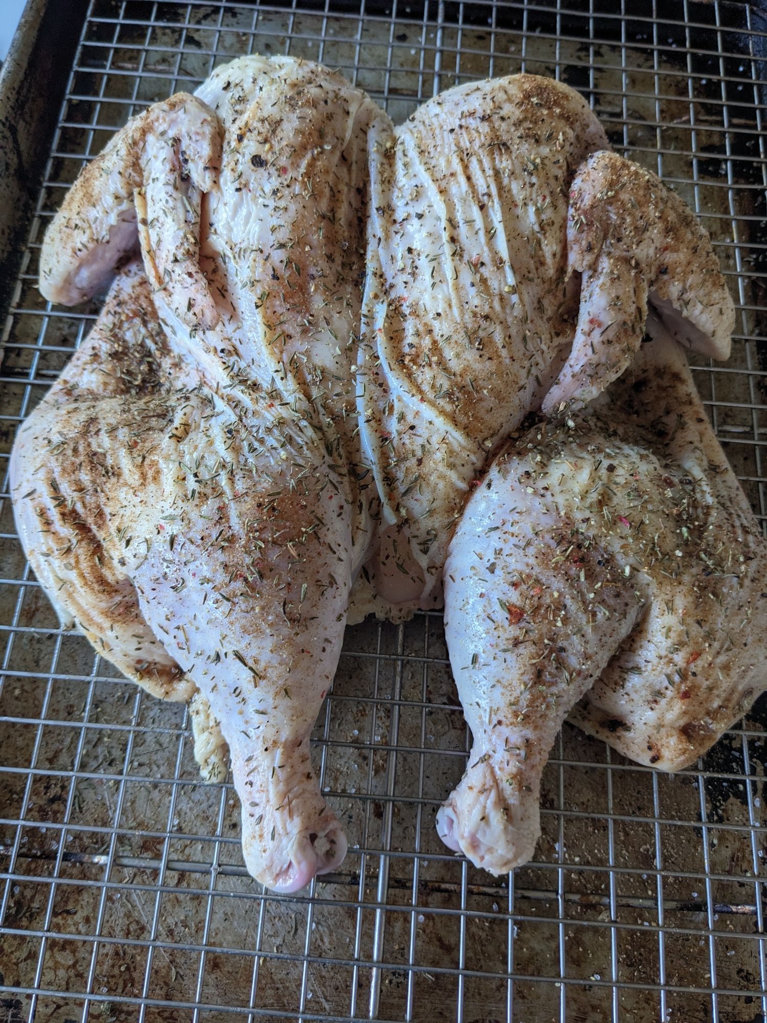 A picture of a seasoned and spatchcocked chicken ready to go in the oven.