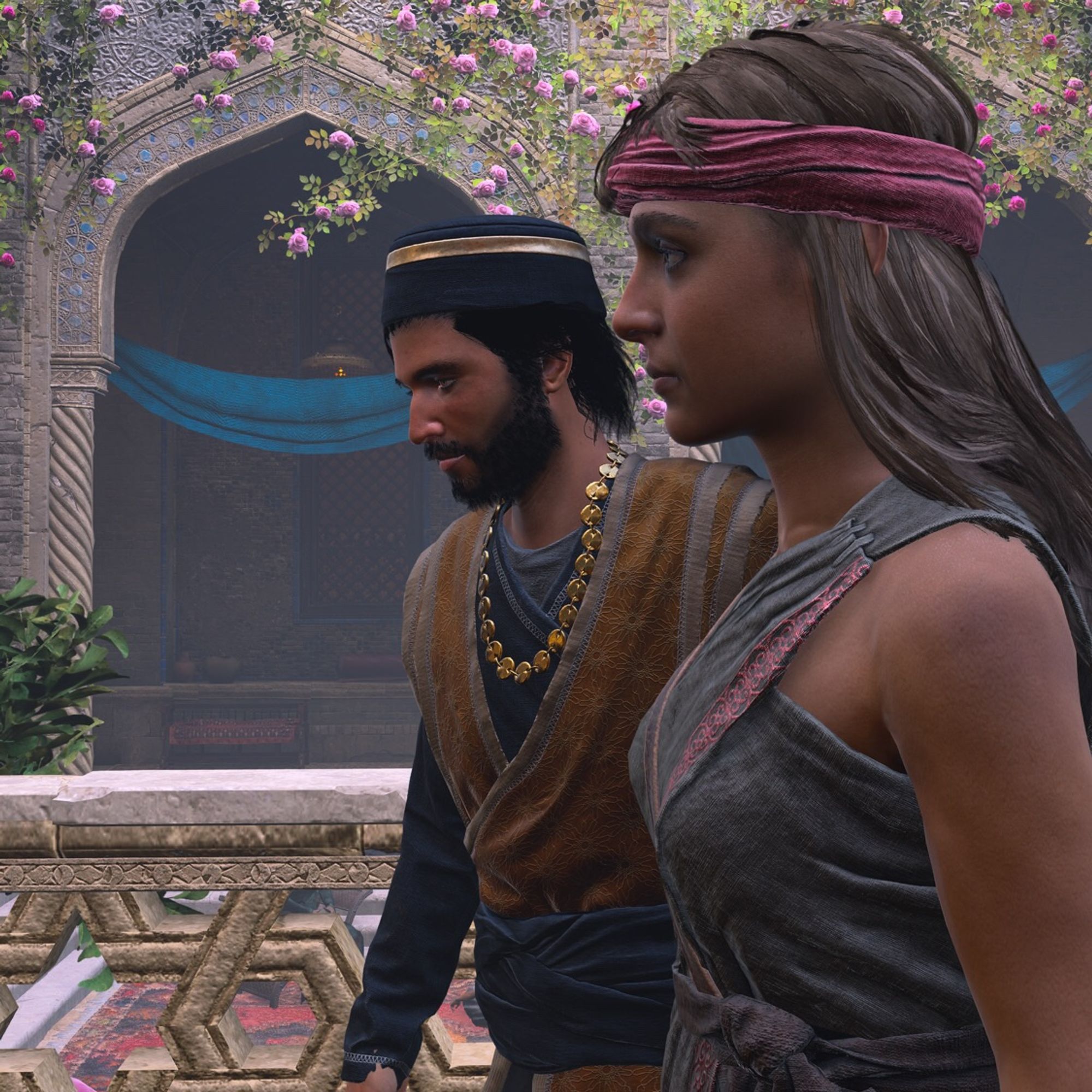 Basim disguised in a eunuch tunic, next to the conniving servant Makira. Flowers and decorative arches in the background.