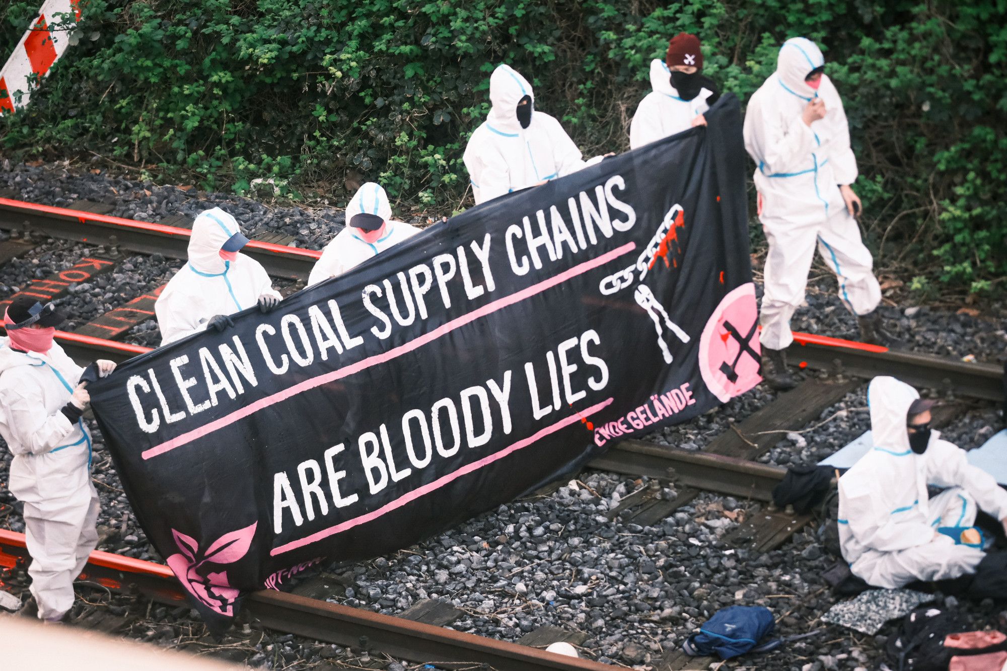 Aktivisti auf rot angemalten schienen. Zwischen ihnen ein transpi mit dem Text: Clean coal supply chains are bloody lies