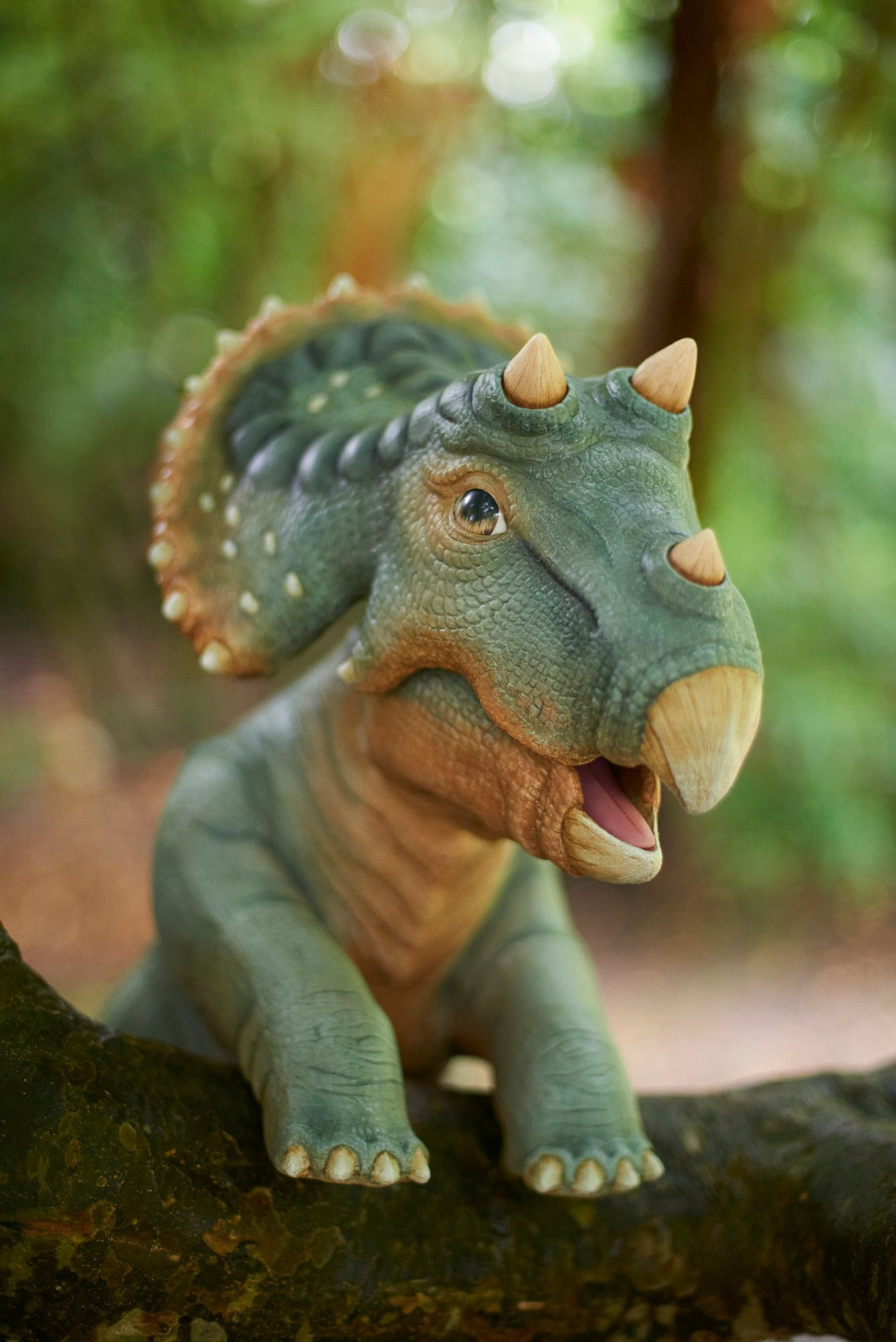 A baby triceratops puppet with green and tan colouration posed leaning over a tree branch