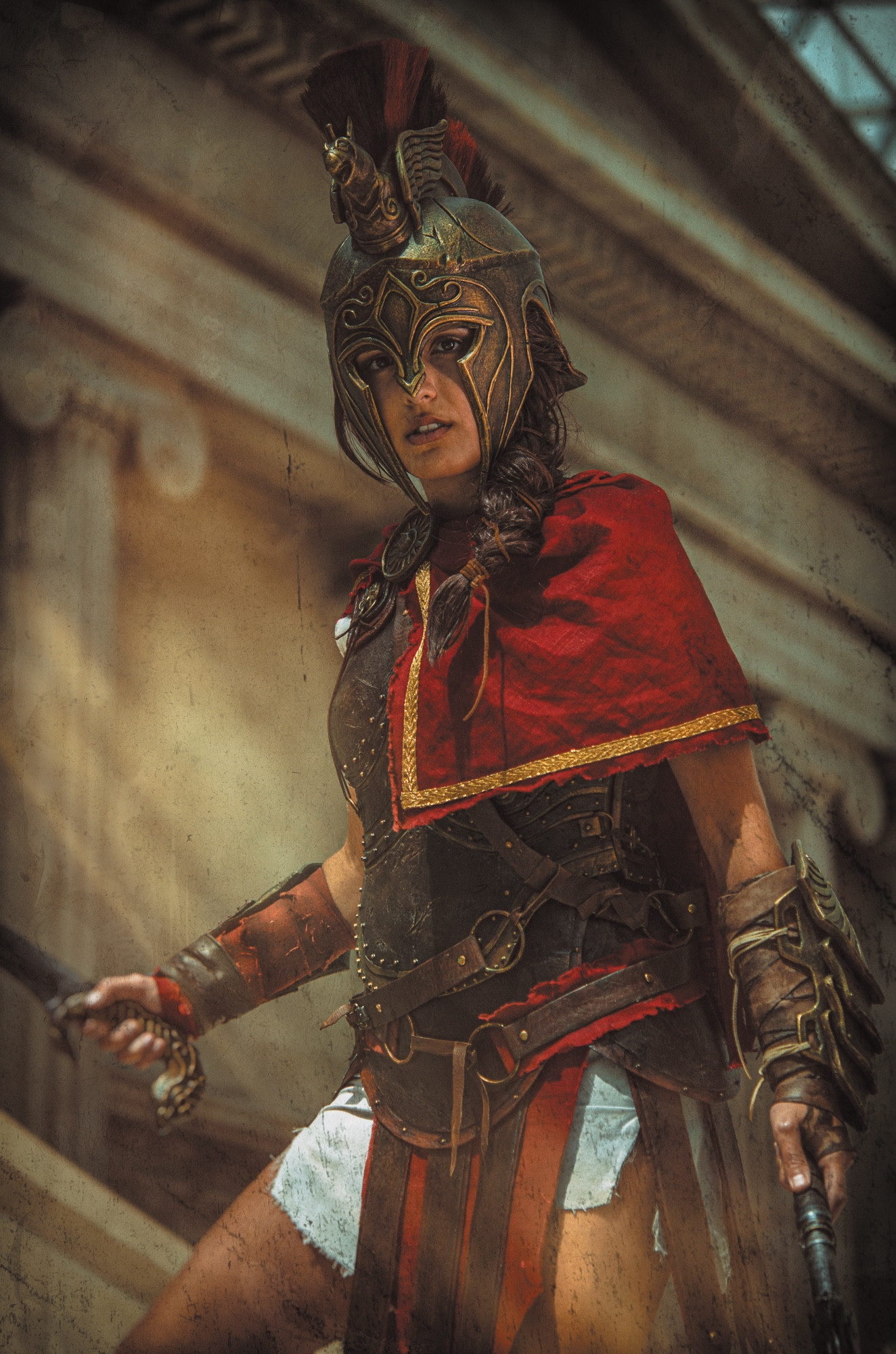 A woman wearing a cosplay of Kassandra from Assassin’s Creed Odyssey: Greek leather armour with a red shawl and gold helmet 