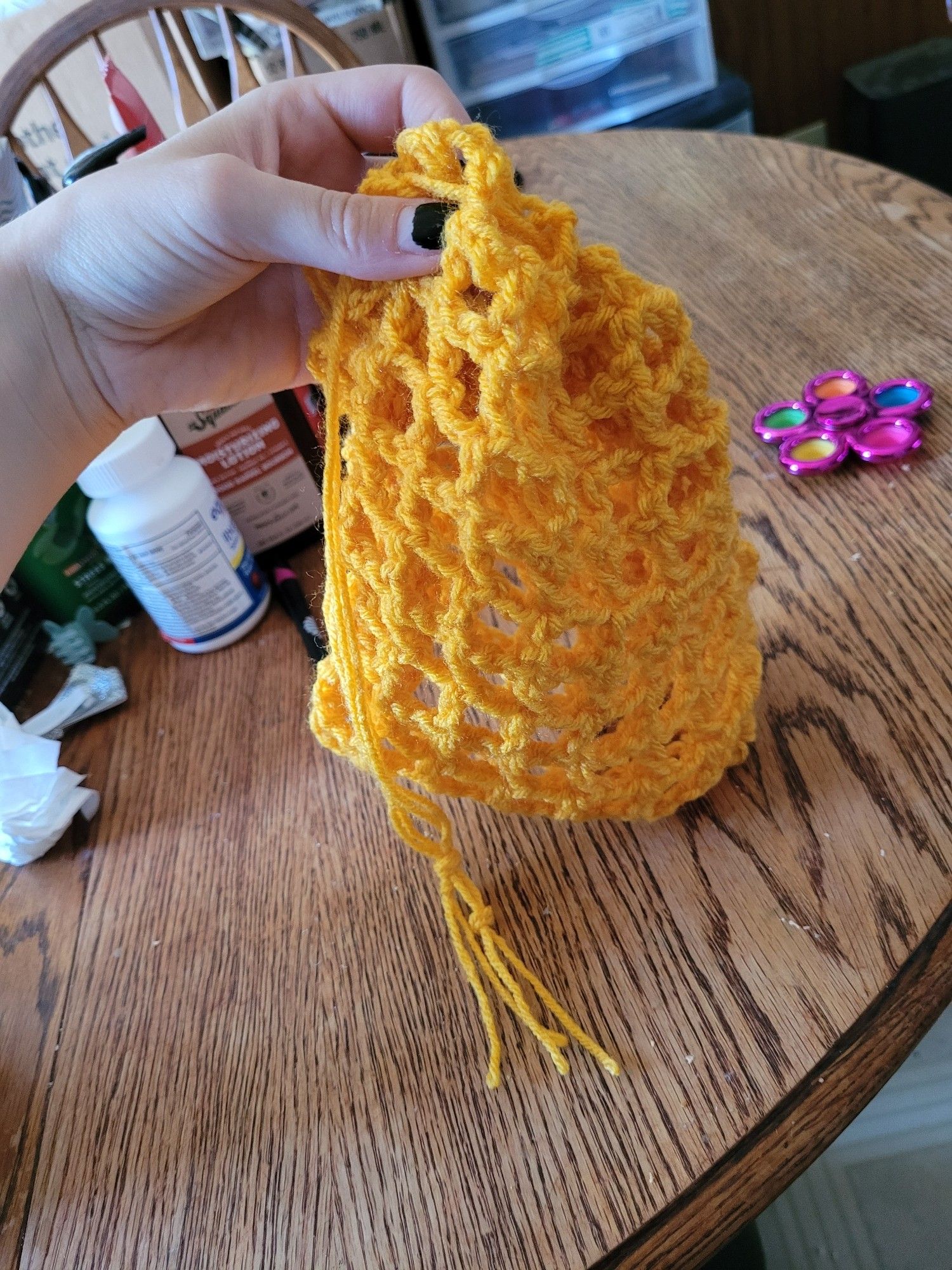 A hand holding up a yellow crochet bag. Background is my kitchen table