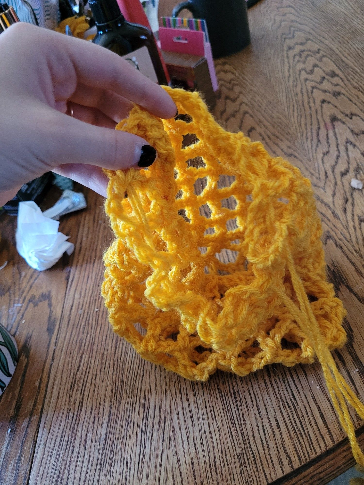 A hand holds open a yellow crochet bag. Background is my kitchen table