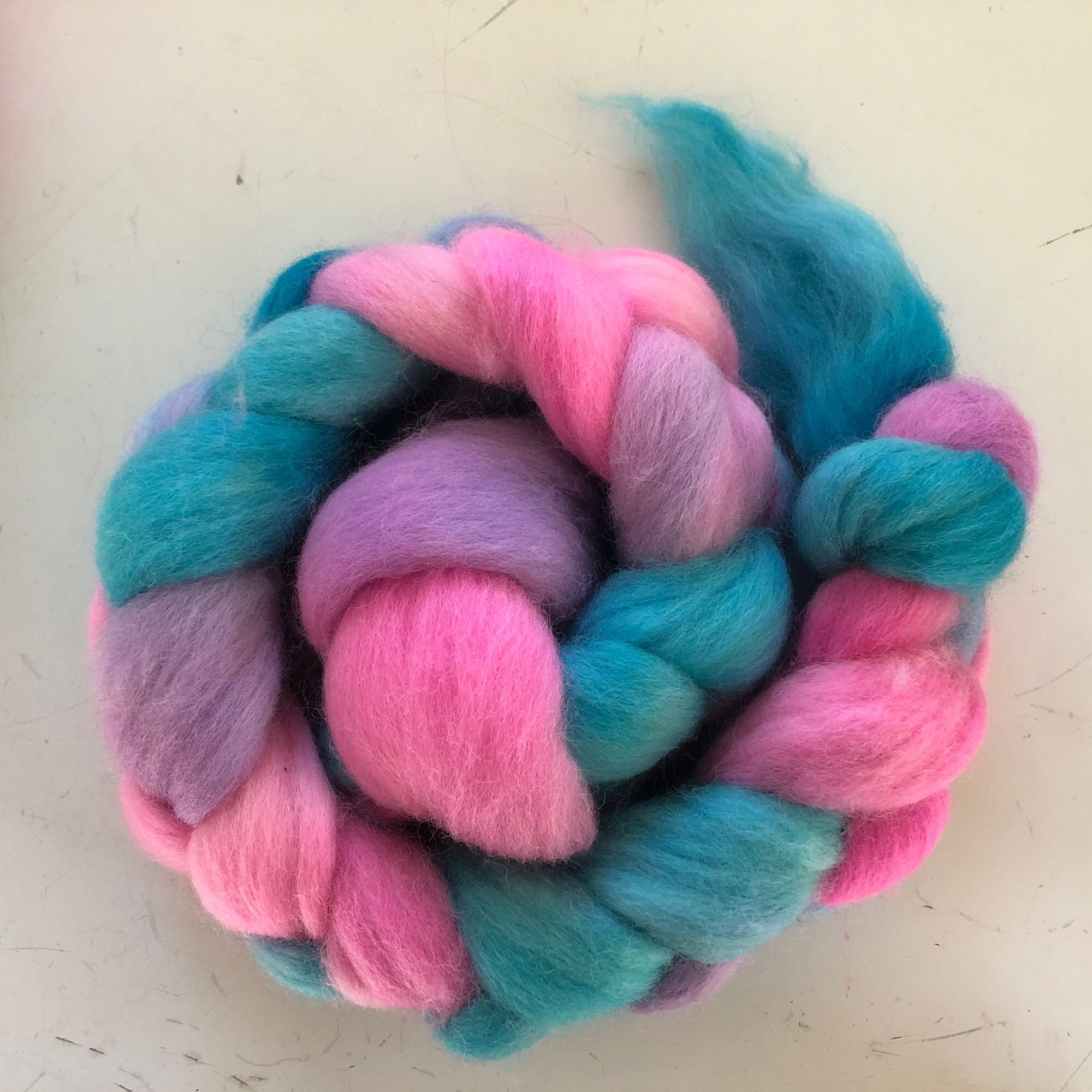 Roving in a braid spun into a spiral. The colors are teal, pink, and slight gradients of purple.