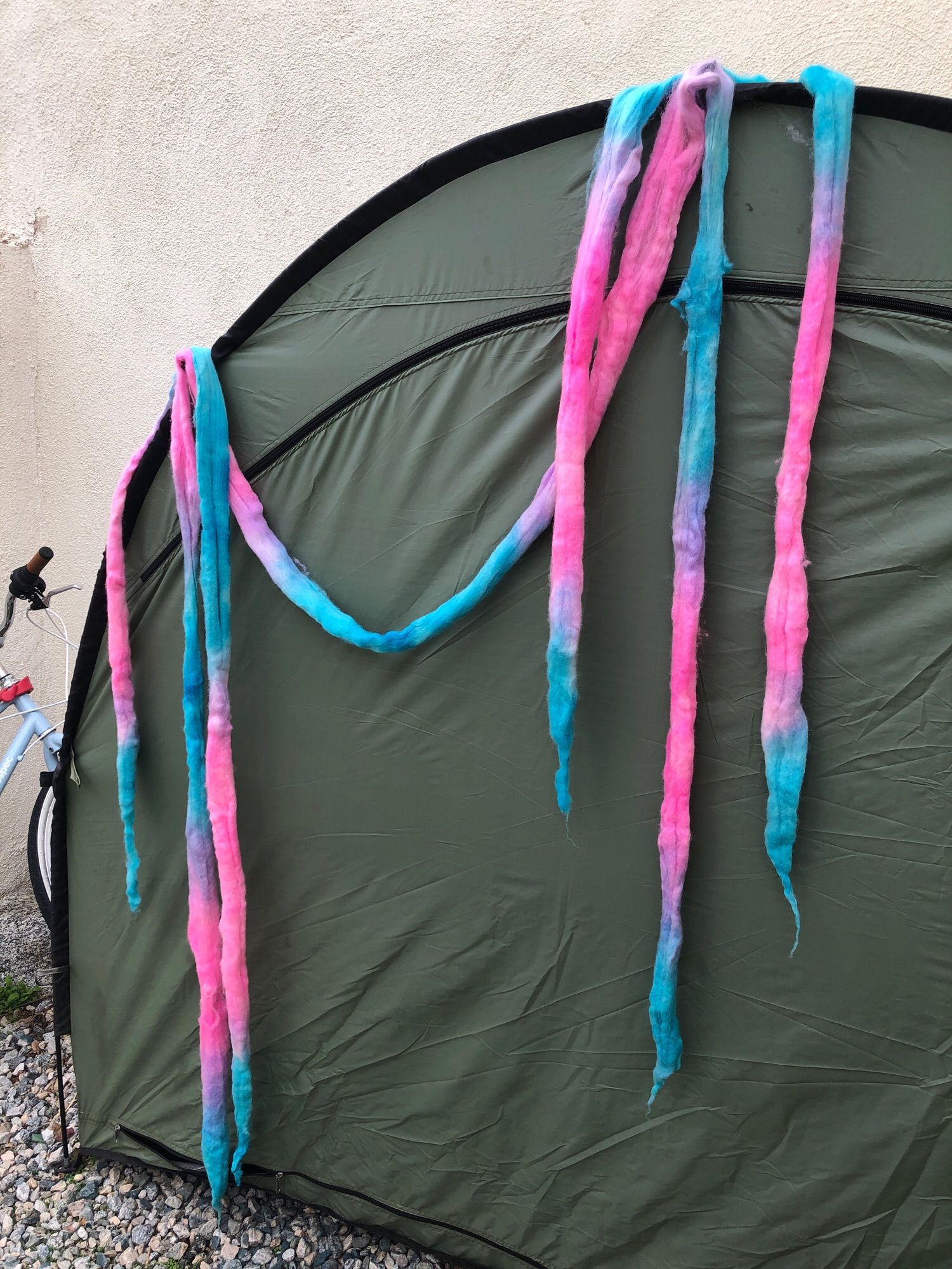 Roving hanging ti dry outside on a bike storage tent. The roving is blue and pink!