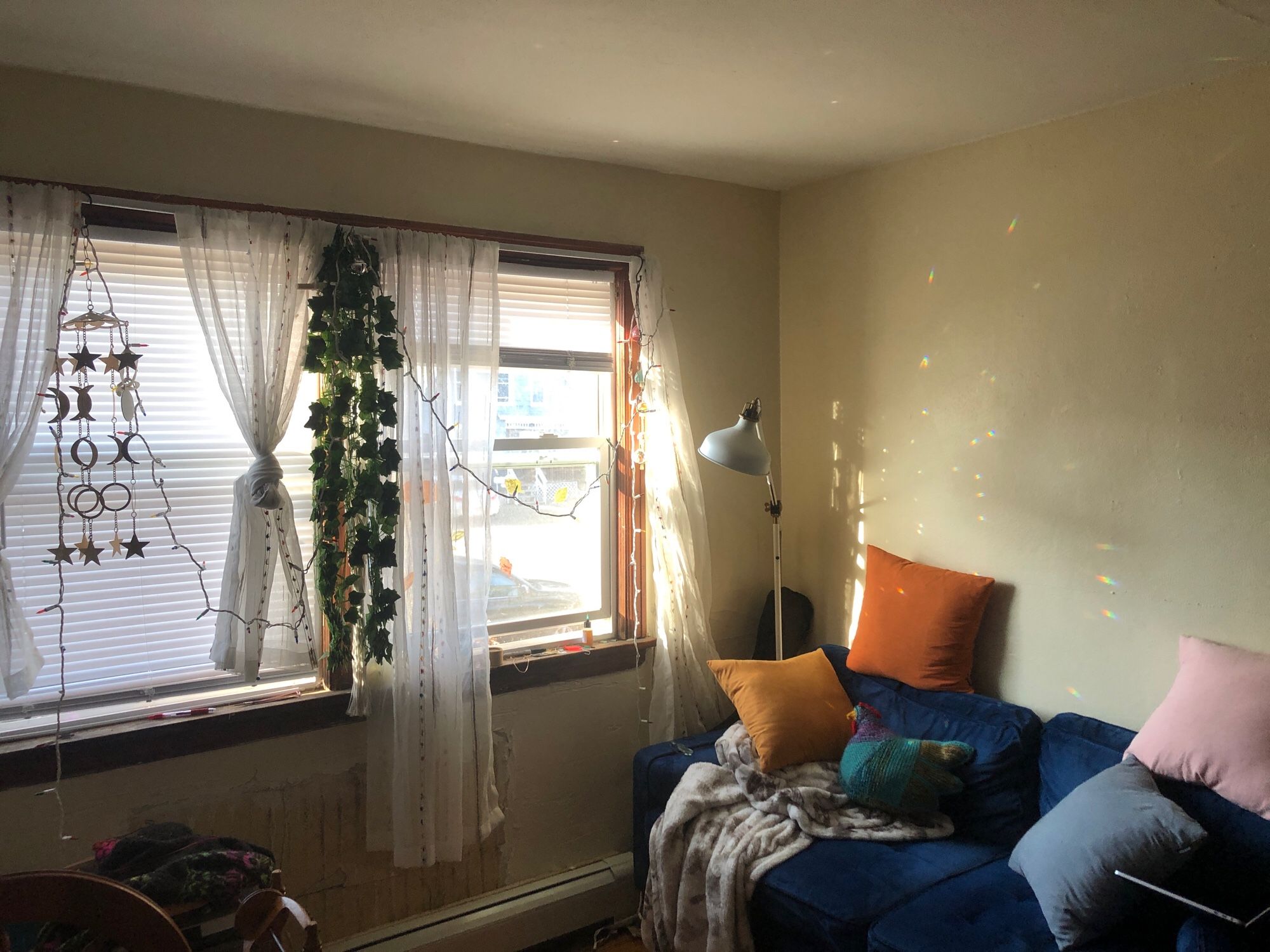 A picture of my couch which sits under a window. There is a beam of light streaming through which is being caught by a light catcher. The light catcher is throwing rainbow specks across the couch.