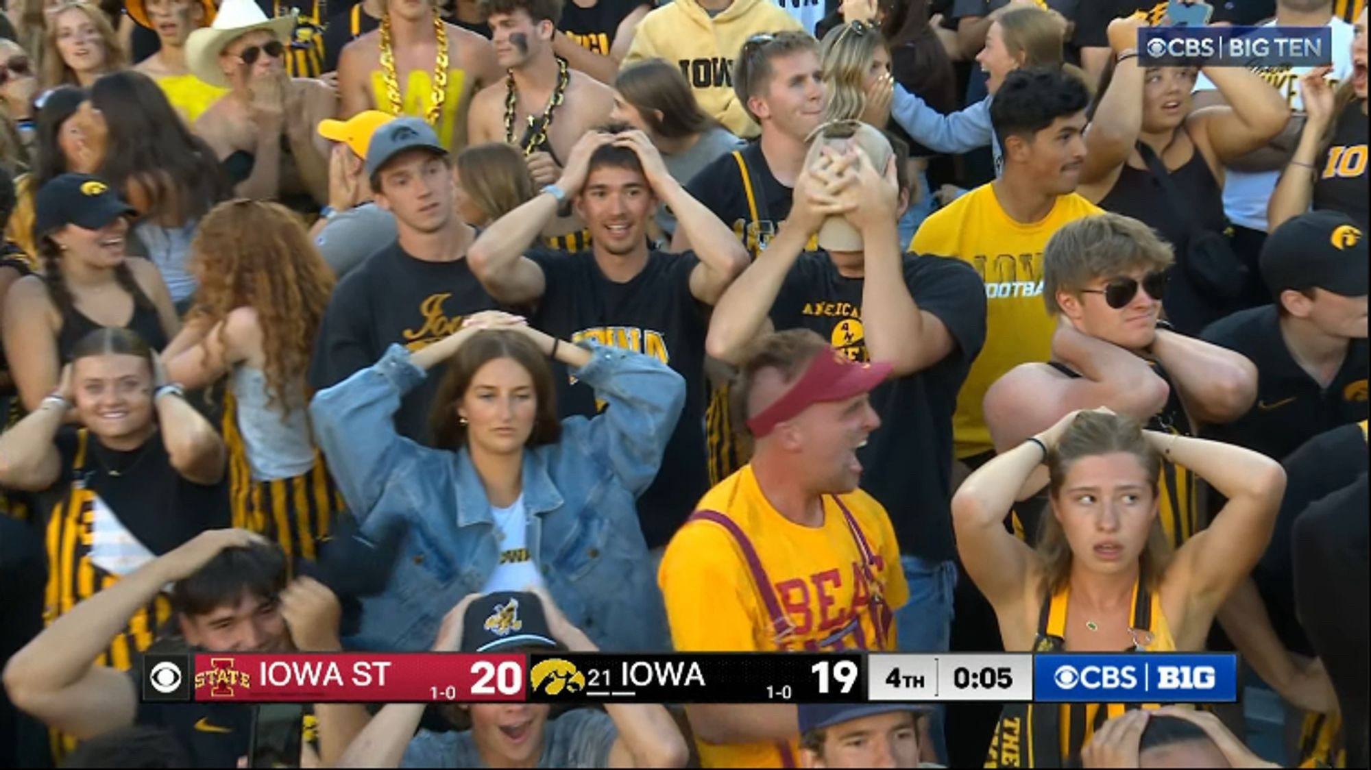 Football fans holding their arms in the “surrender cobra” gesture. The score reads Iowa St 20, Iowa 19.