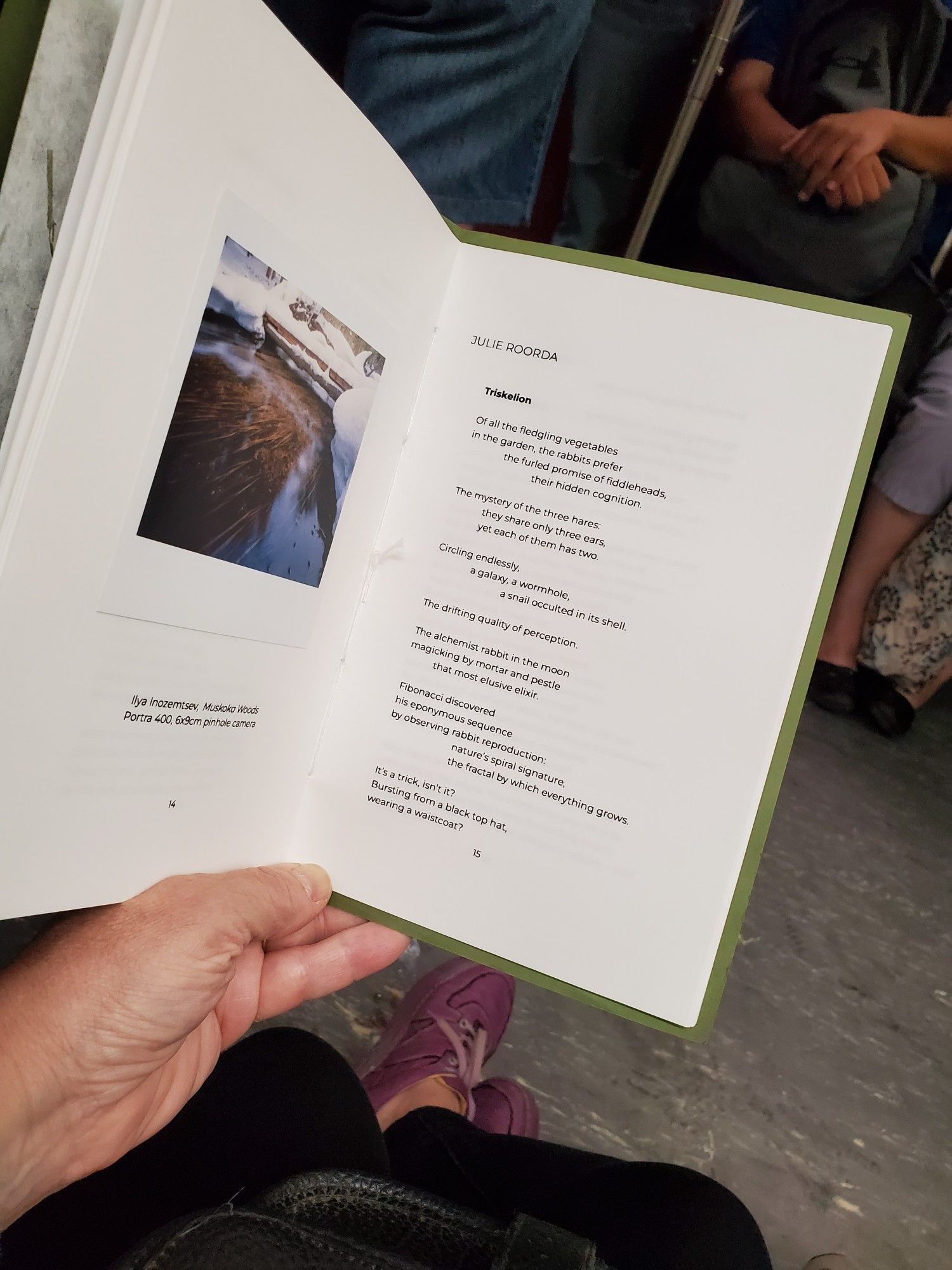 Reading a poem by Julie Roorda from the poetry collection/chapbook Pinhole Poetry Volume One Selected while riding the subway, with subway seats and passengers visible in the background