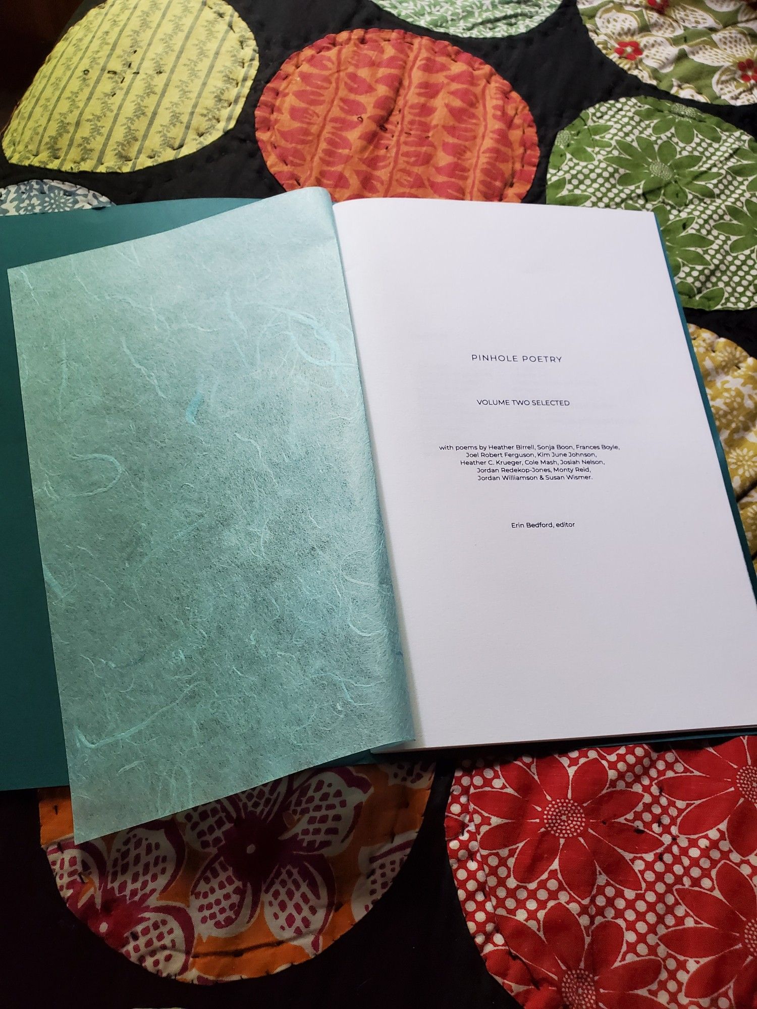 The poetry collection/chapbook Pinhole Poetry Volume Two Selected sits on a colourful quilt.