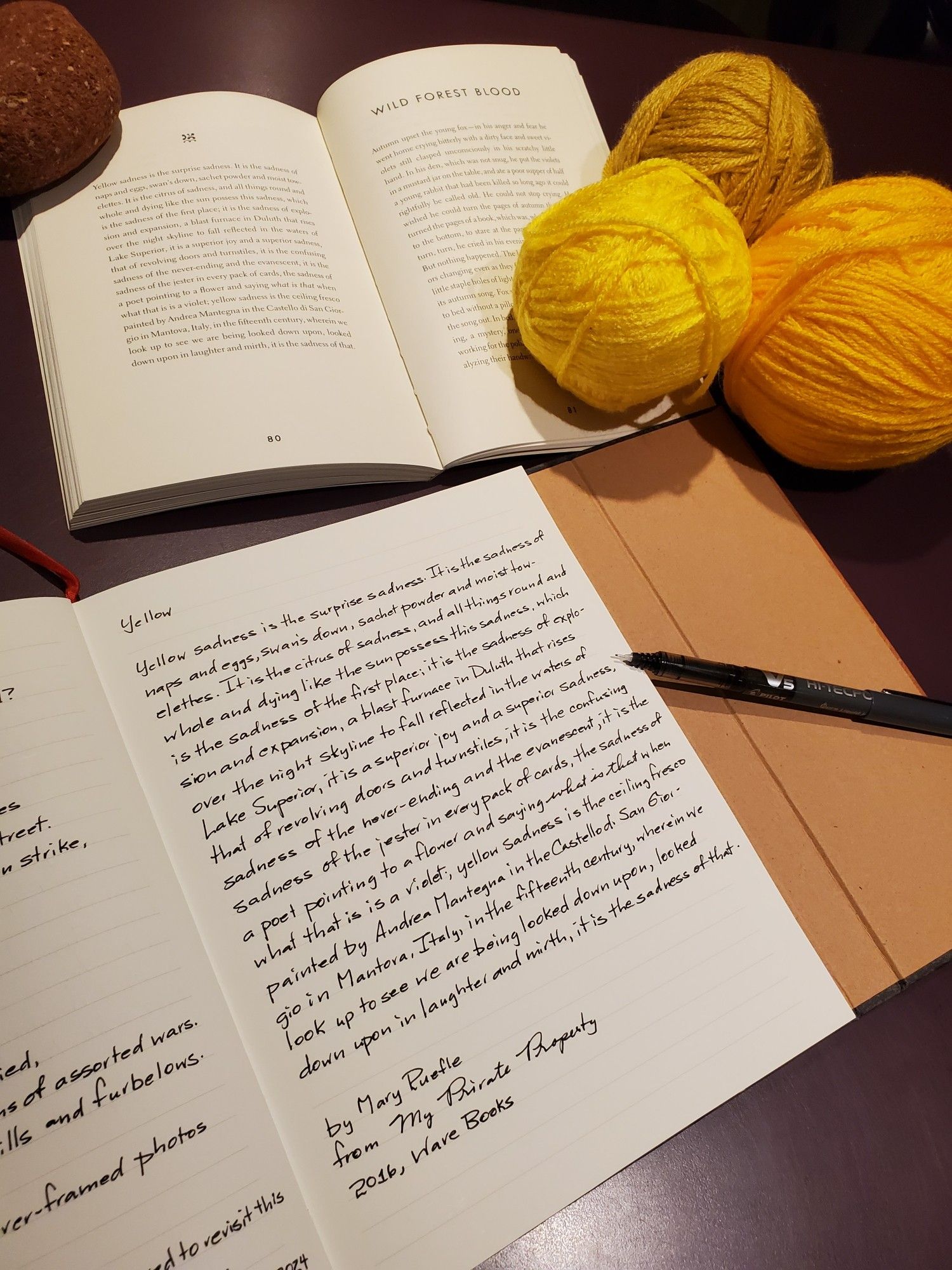 Handwritten transcription of the poem "Yellow" by Mary Ruefle from the poetry collection My Private Property - the book is held open with a piece of red brick, an uncapped black pen rests on the notebook page and balls of yellow wool nestle nearby