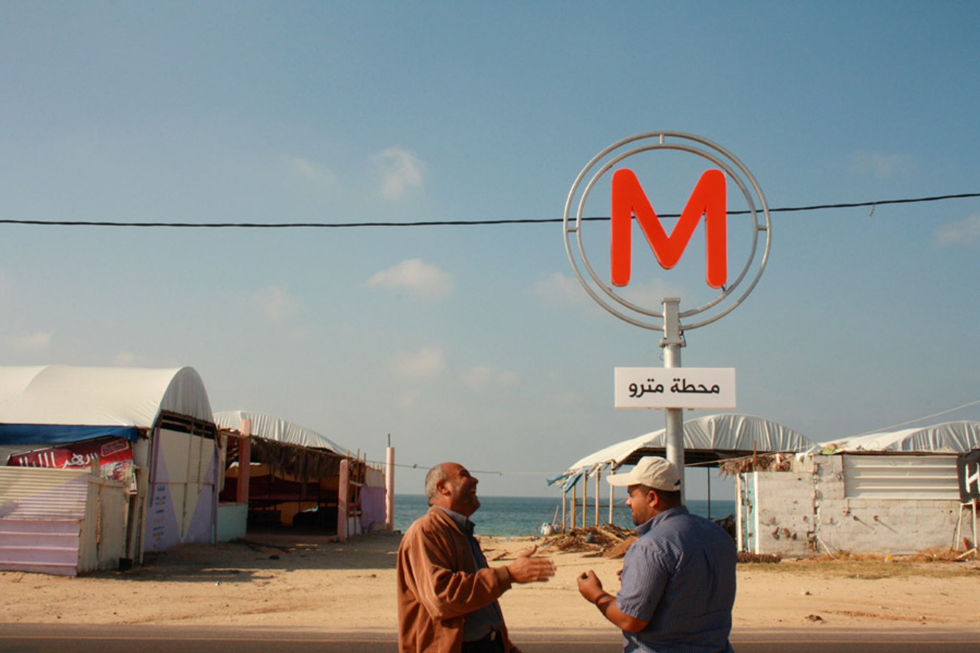 Photo shows two men laughing under a Metro sign in Gaza, as part of an art photography project by the artist Mohamed Abusal.