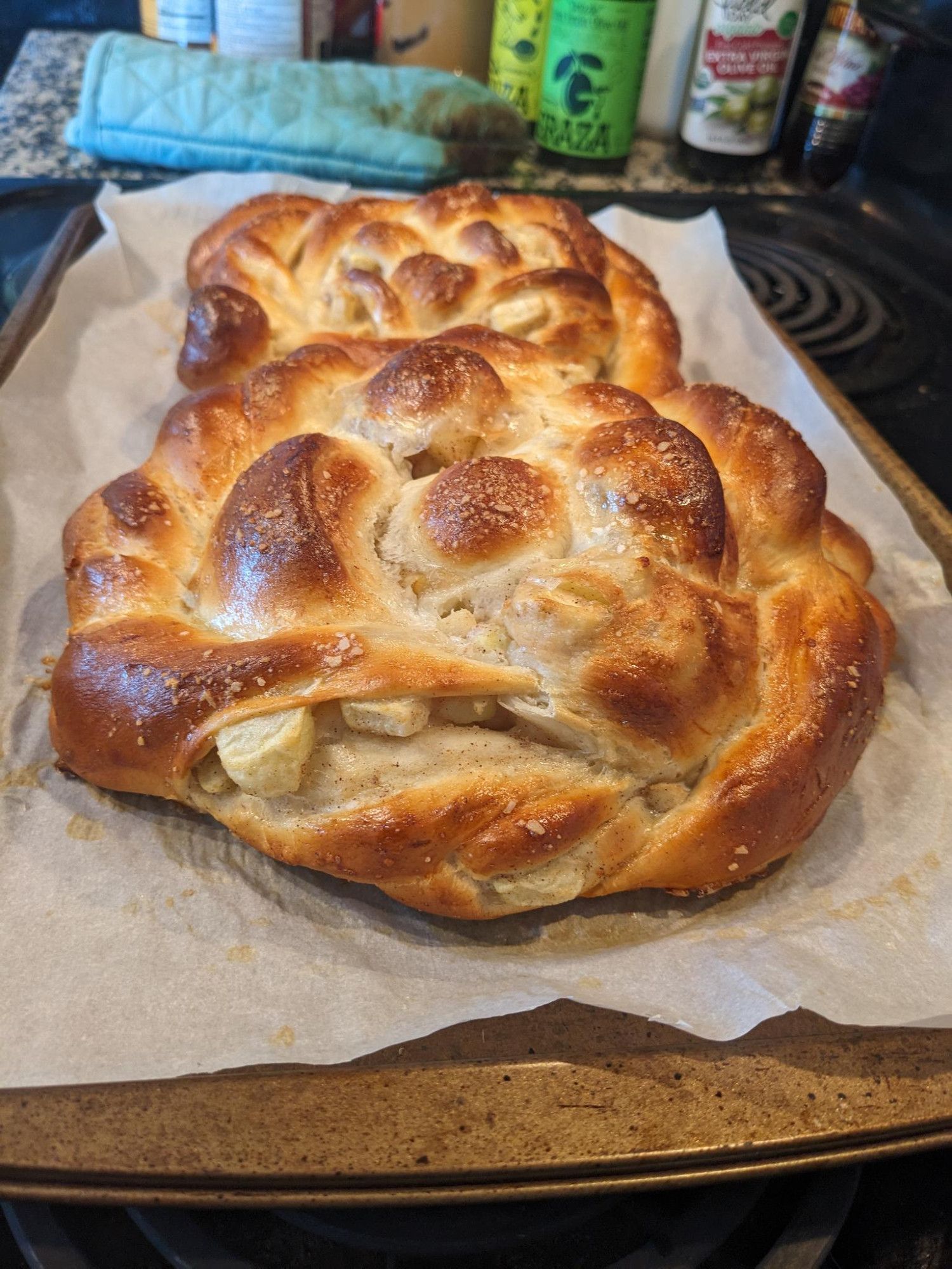 Two round challot cooling on a baking sheet. One of the braids has split at the seam (sadly) exposing chunks of apple inside.